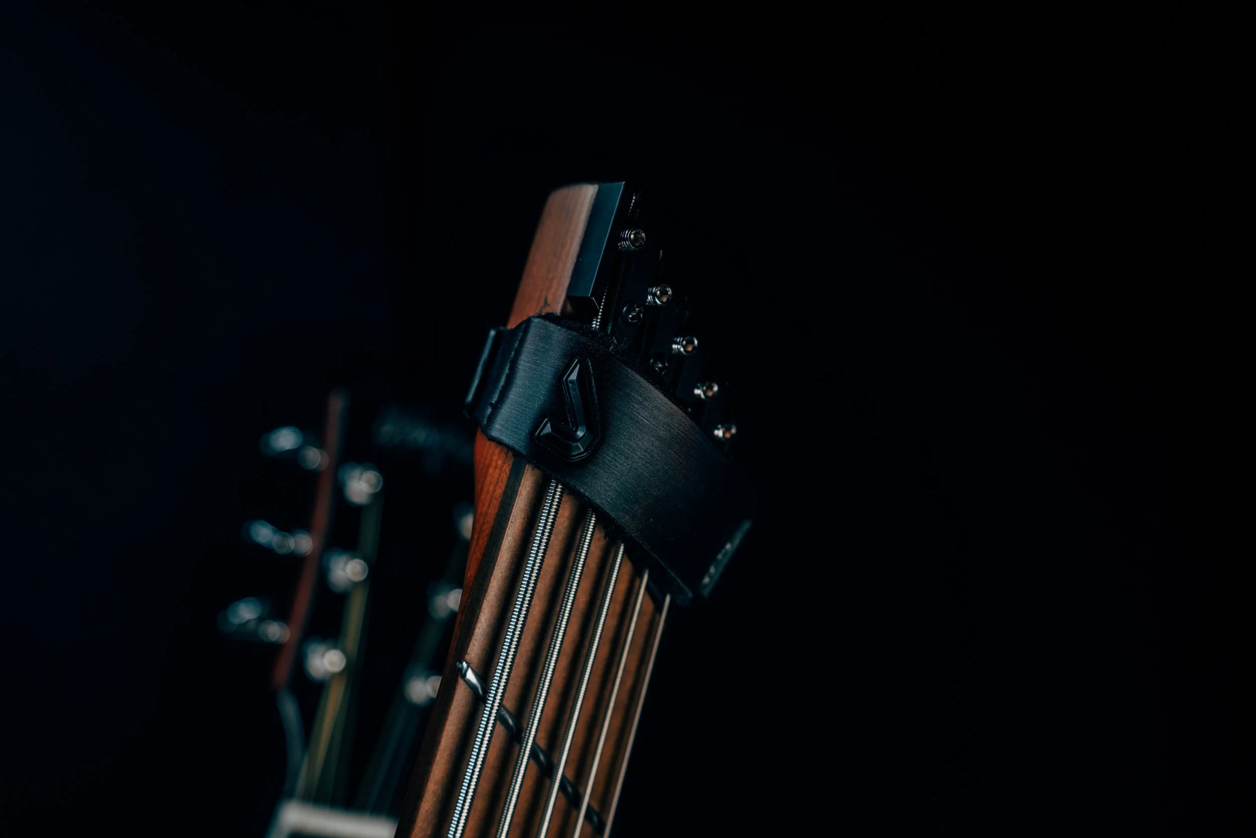 Close-up of the headstock of an electric guitar with a black strap against a dark background.