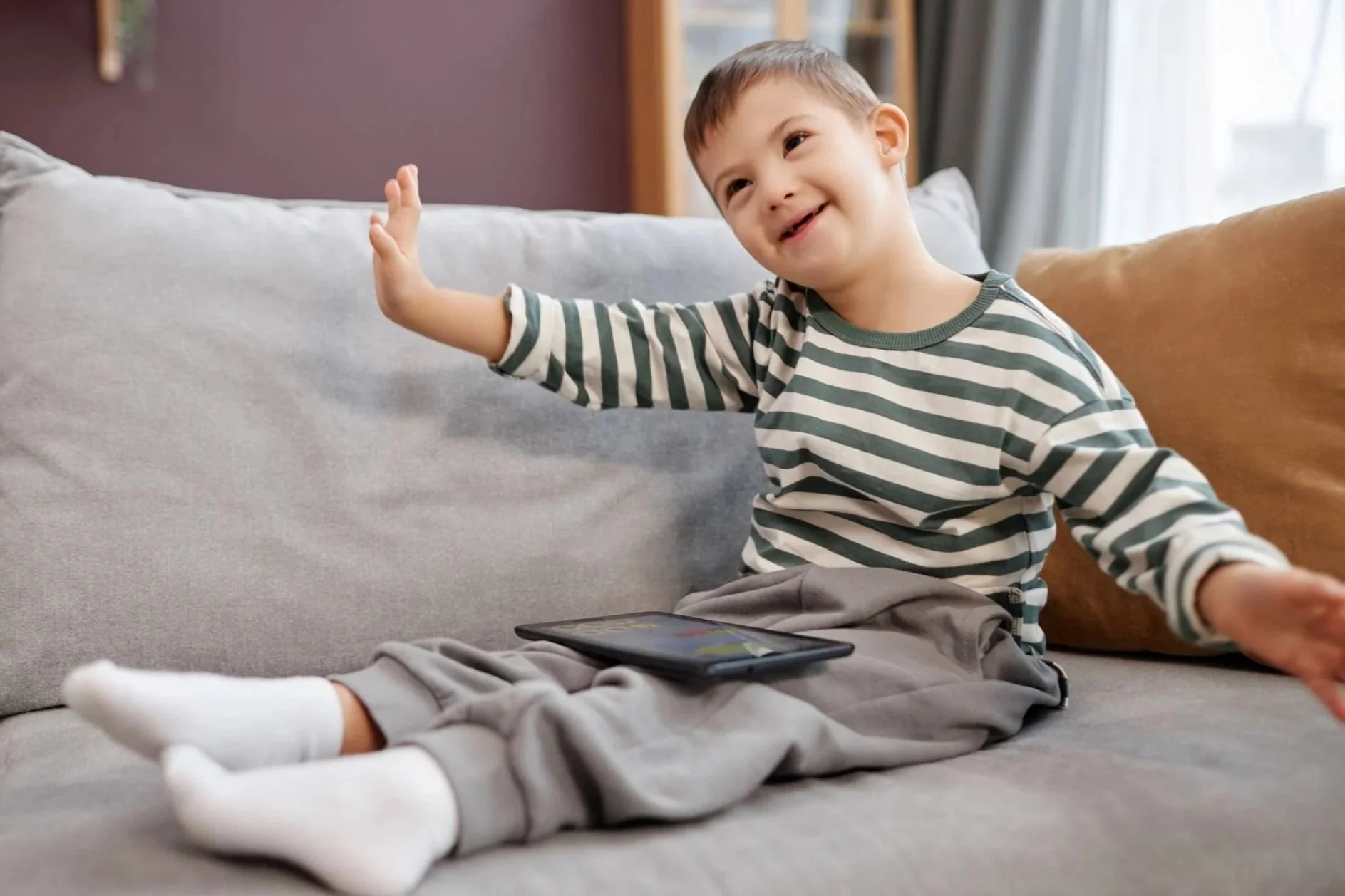 Smiling boy with Down Syndrome uses his AAC device at home