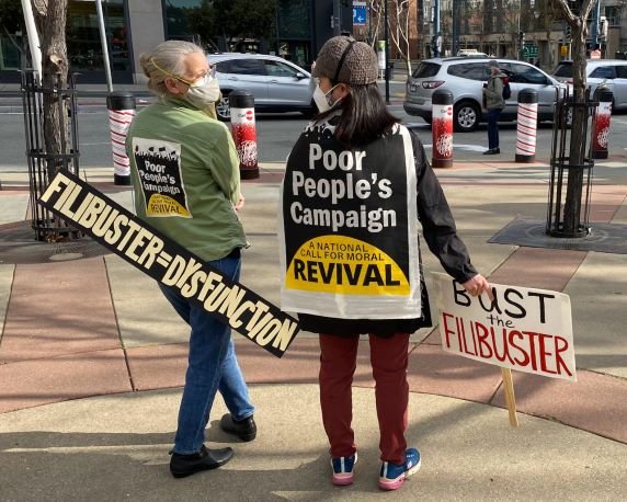 Two demonstrators with signs reading "Filibuster=Dysfunction" and "Bust the Filibuster"