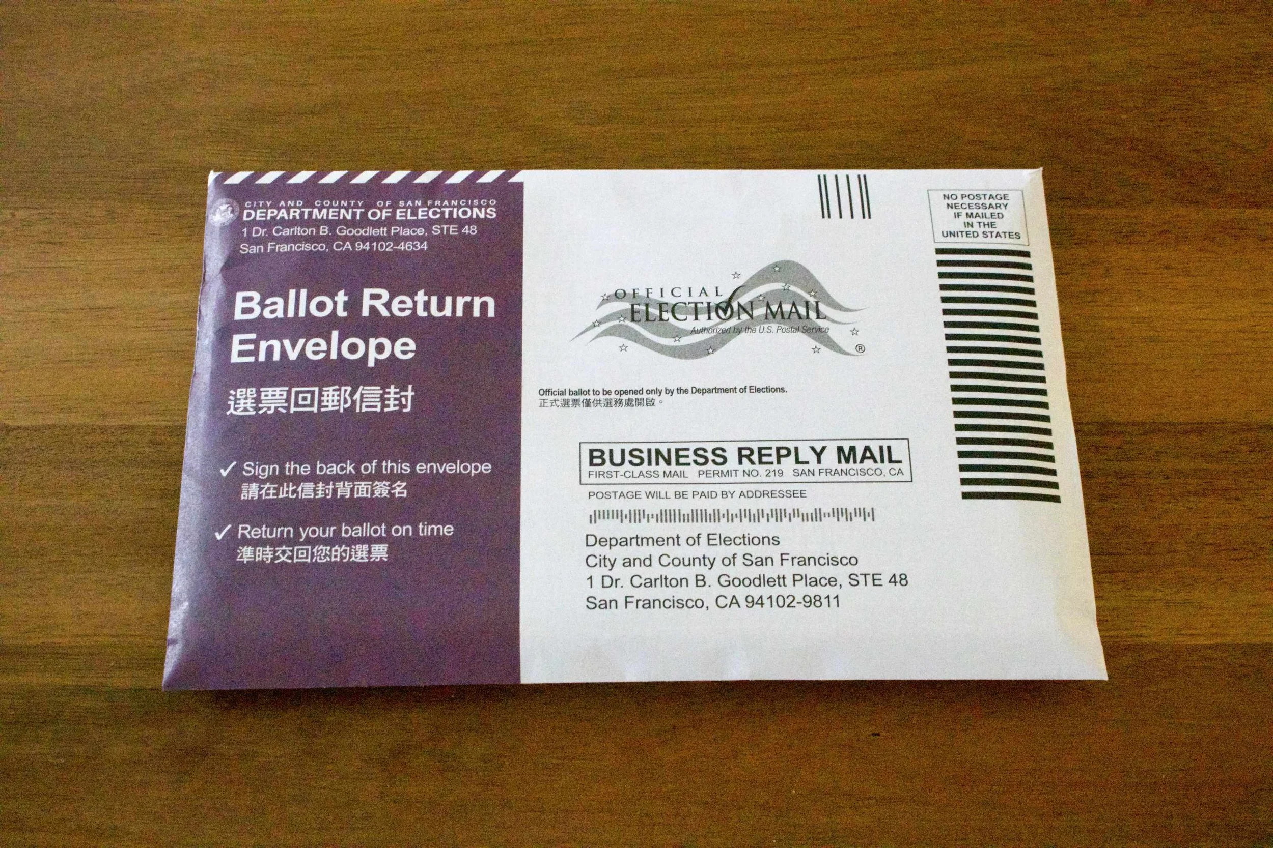 The front of the ballot return envelope, which says “Ballot Return Envelope” in white on a purple field and is addressed to the Department of Elections under the “Official Election Mail” insignia.