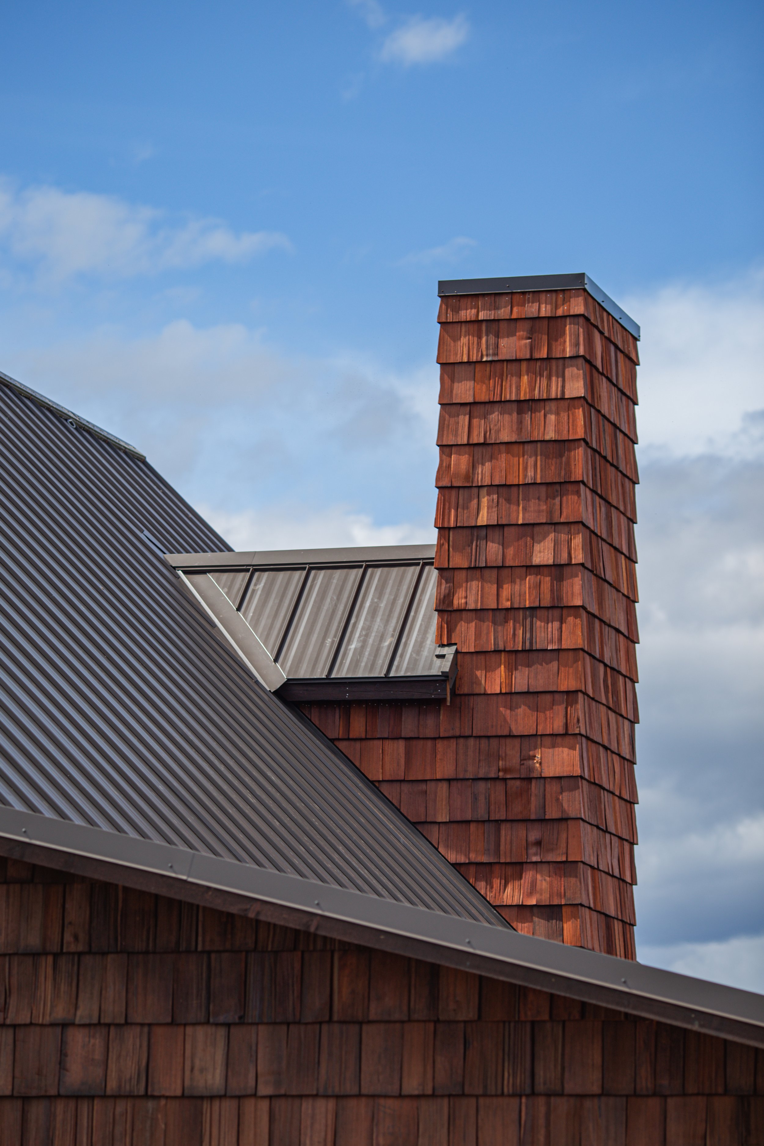 A residential building with a metal roof and a prominent red brick chimney against a partly cloudy sky.