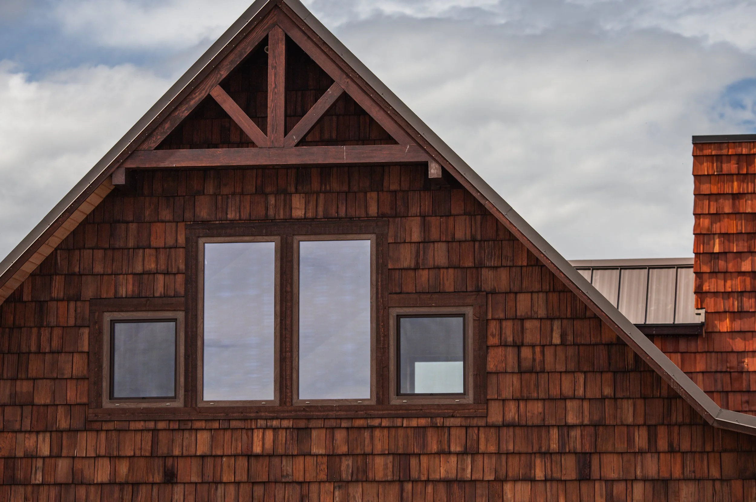 Ellensburg Ranch House, Close-up of a gable roof with wooden shingles and window on a house, with a cloudy sky in the background.