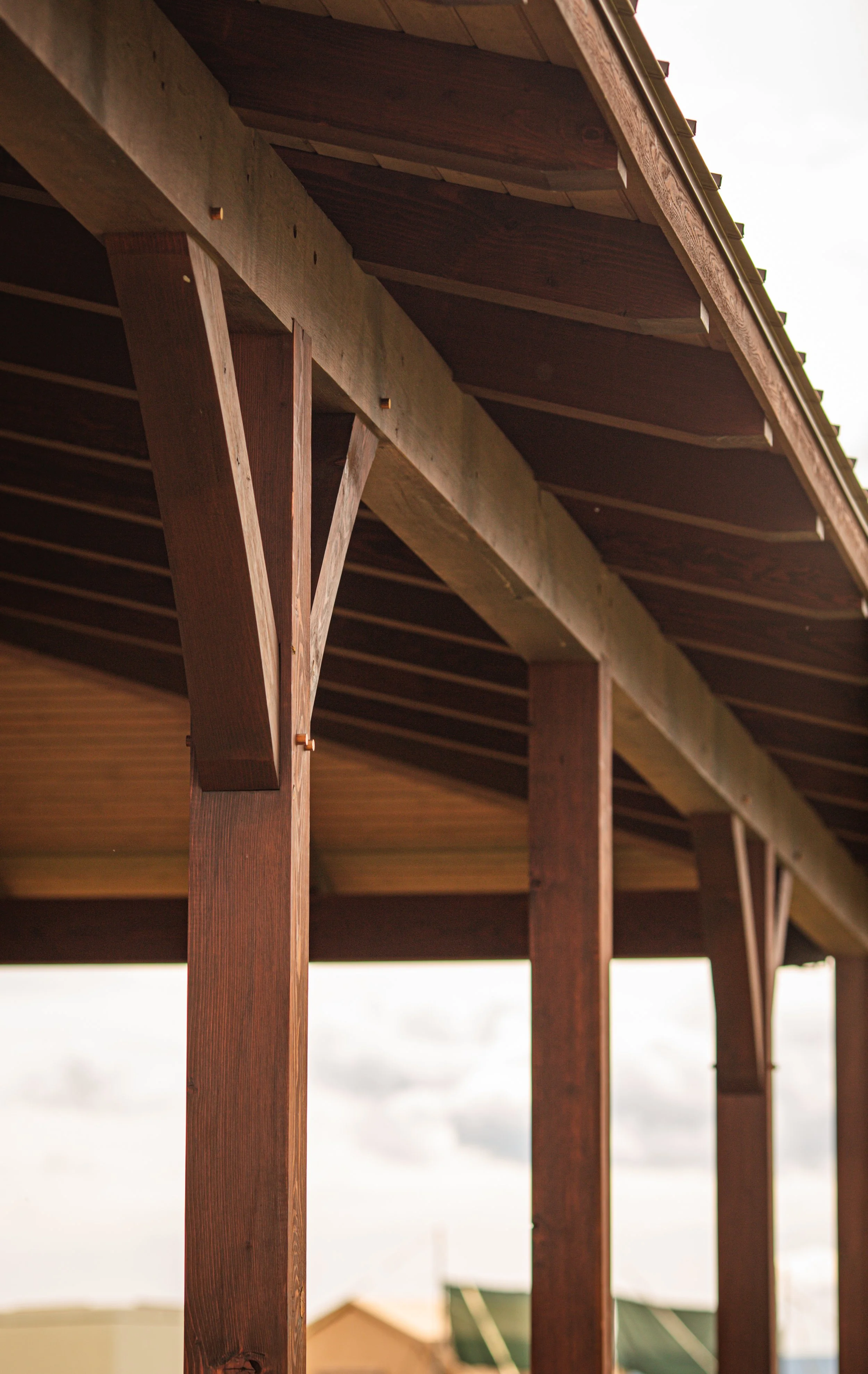 Close-up view of wooden beams supporting a roof structure, with a cloudy sky and rooftops in the background.