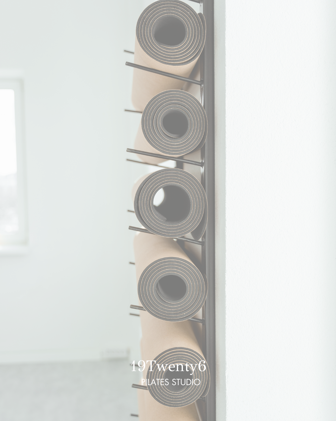 Four rolled yoga mats mounted on a black wall rack against a white wall in a bright room.