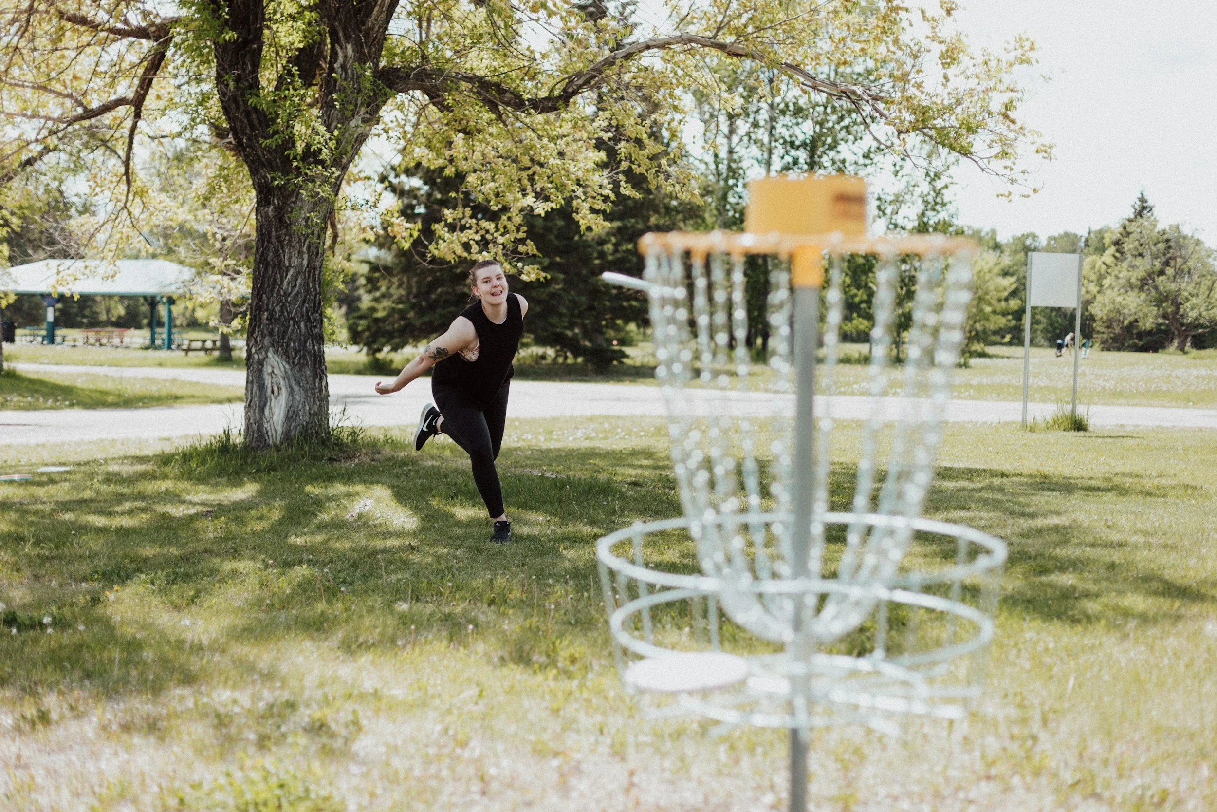 A woman playing disc golf outdoors in a park, preparing to throw a disc towards a chain basket.