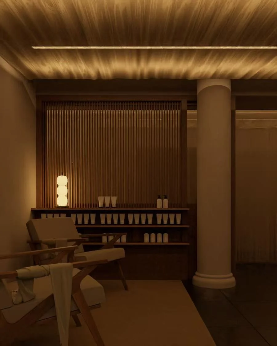 A cozy, dimly lit corner of a room with warm lighting, a wooden chair, a small table, a decorative lamp, and shelves with bottles and containers.