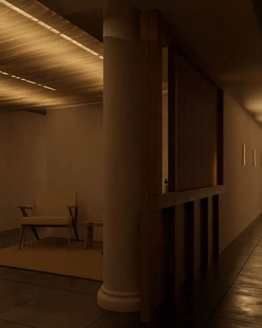 Dimly lit interior space with a wooden bench and small table on a beige rug, partially obscured by a pillar and a wooden partition, with a hallway extending to the right.