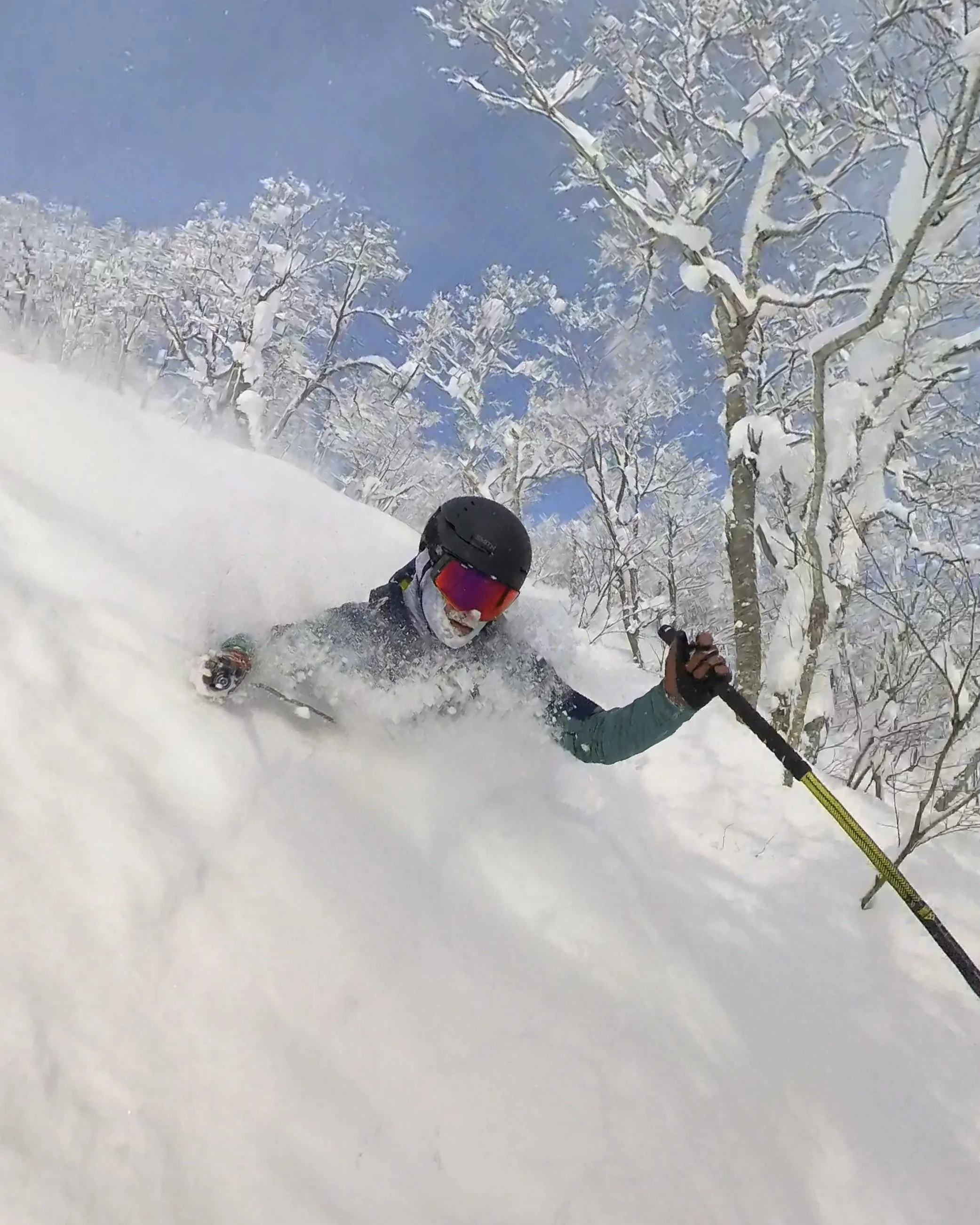 A person skiing through deep snow in a snowy forest under a clear blue sky.