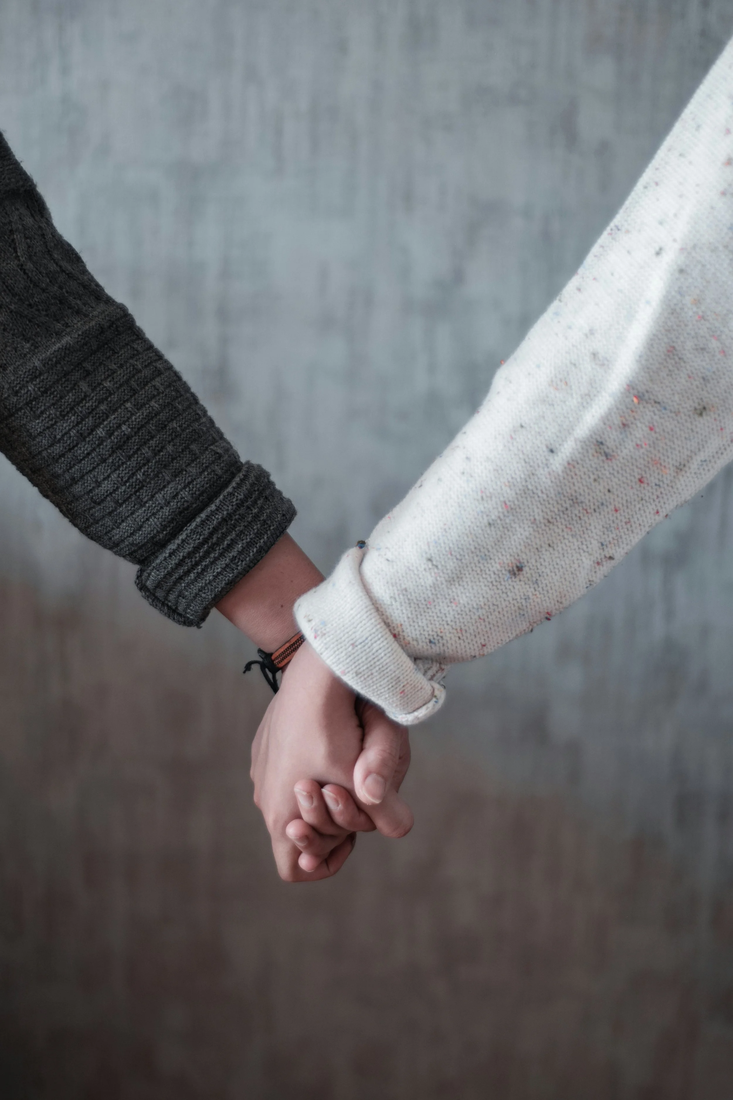 Two people holding hands against a plain gray background.