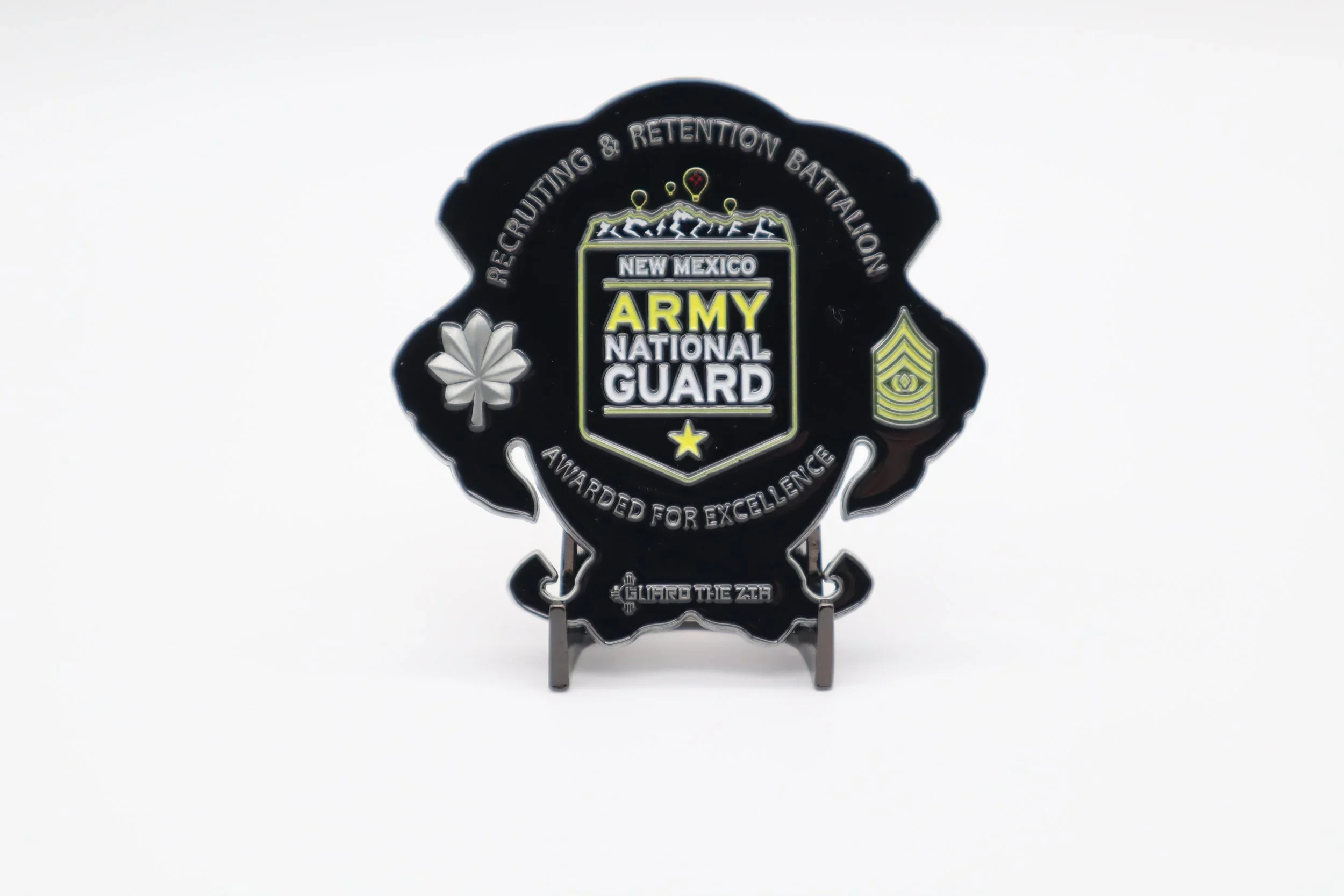 Badge with the emblem of the New Mexico Army National Guard, featuring mountains, animals, snowflakes, a star, an eye, and insignia, with text about recognition and excellence.