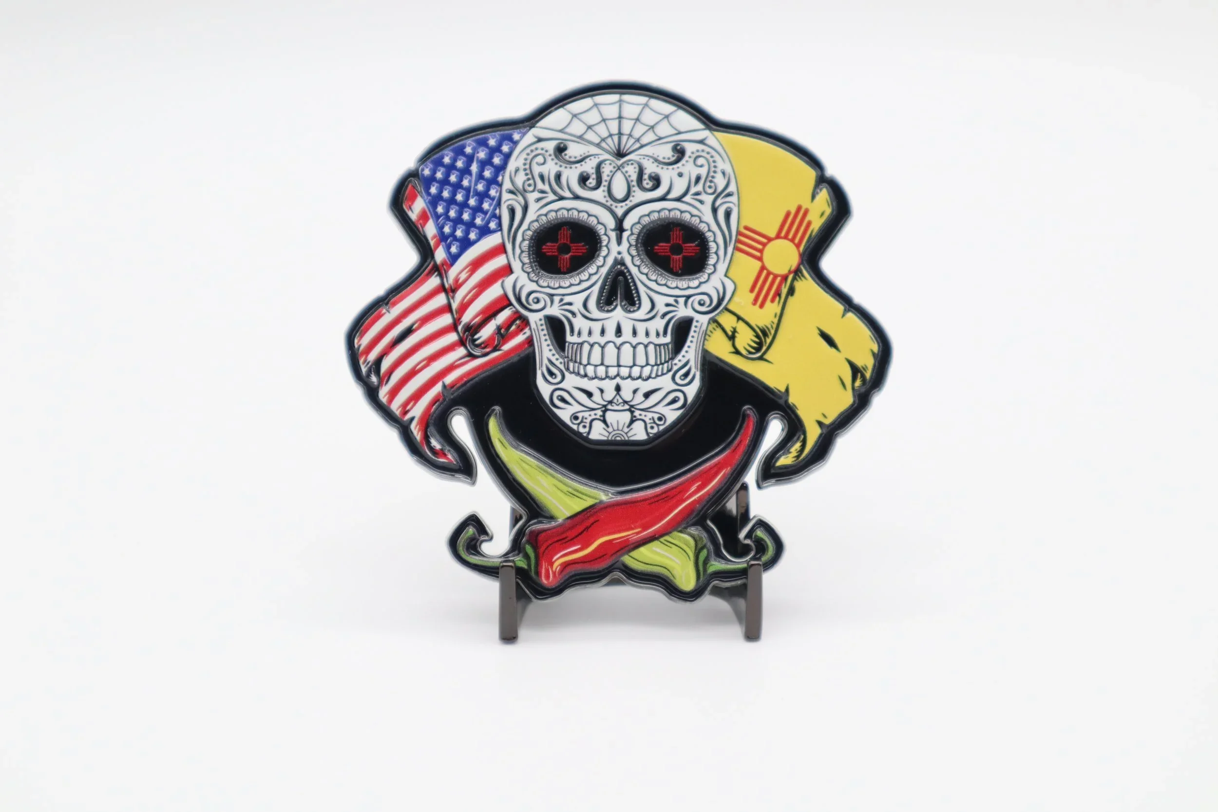 Colorful patch featuring a sugar skull with black eyes and red cross details, flanked by the American and Spanish flags, on a white background.