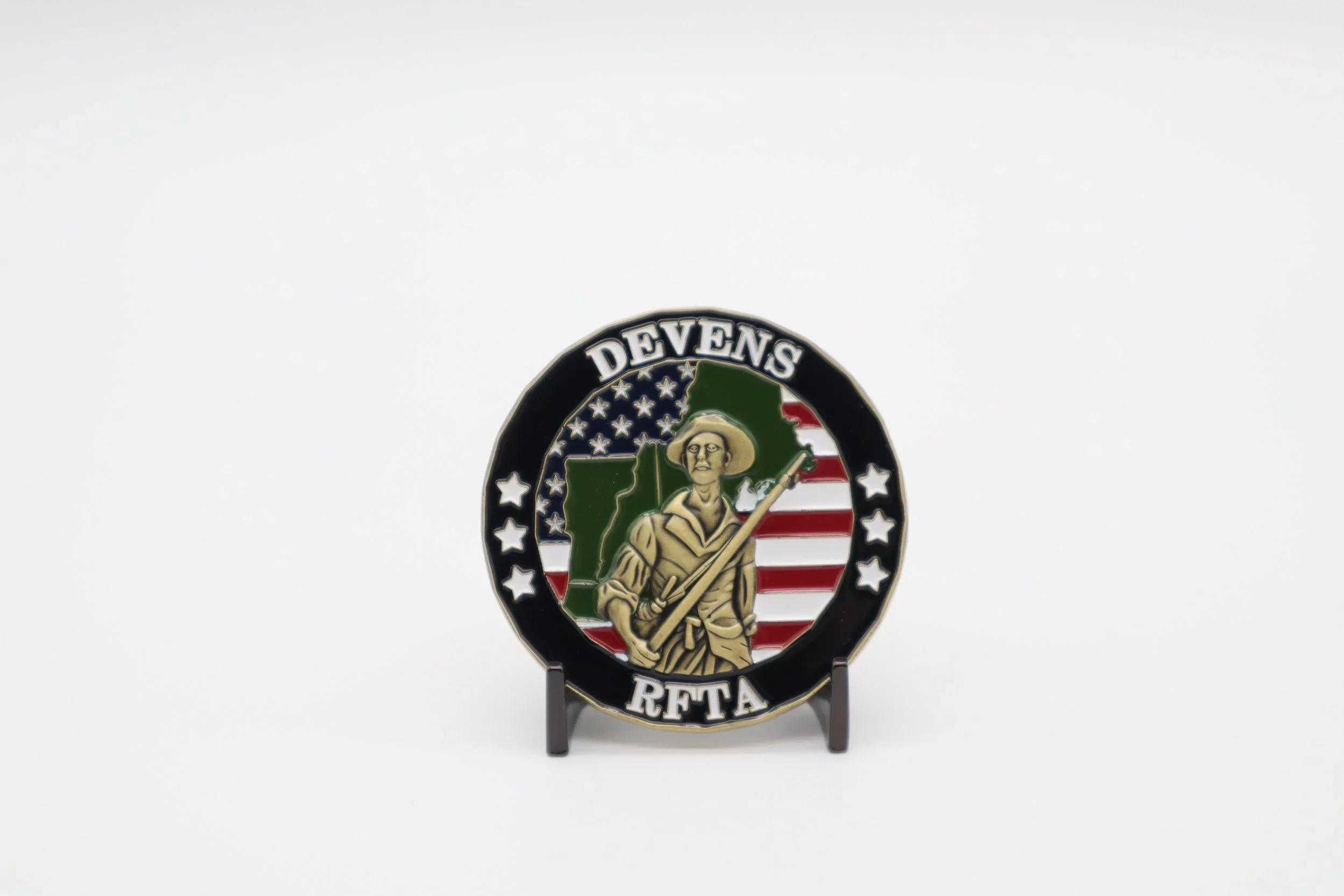 A circular embroidered patch featuring a soldier holding a rifle, with the text "DEVENS" at the top and “RETA” at the bottom, set against a background with the American flag and a green outline of a state.