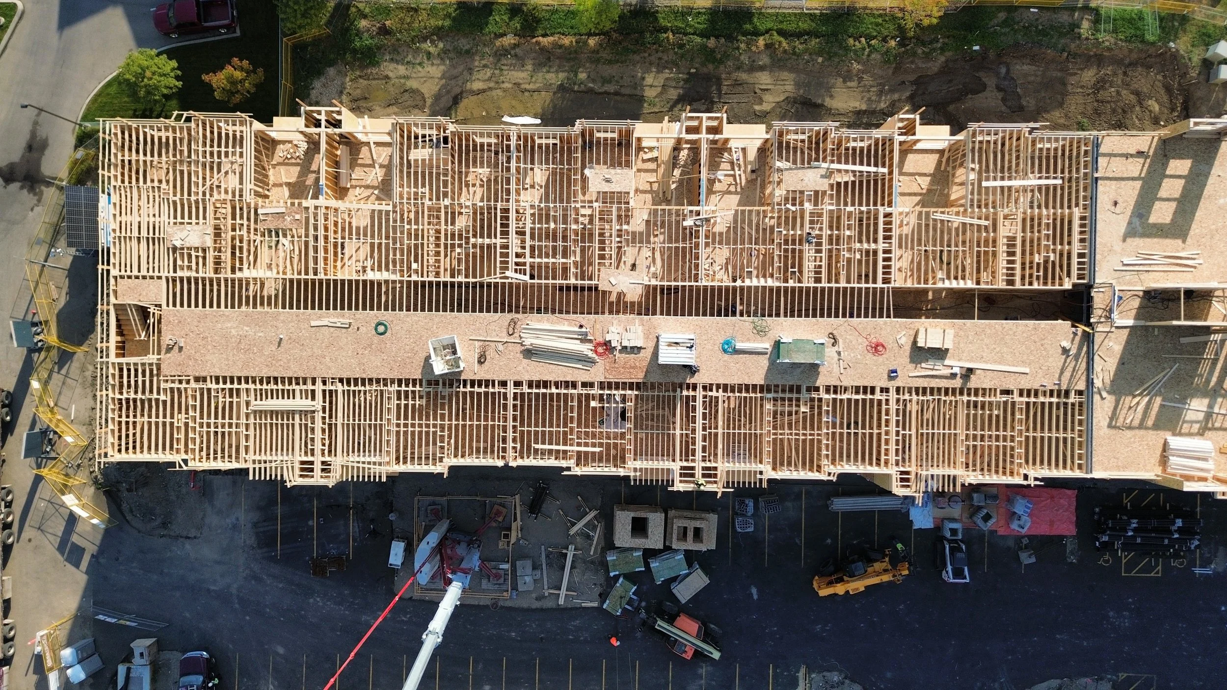 Aerial view of a multi-unit building under construction with wooden framing, construction materials, and vehicles around the site.