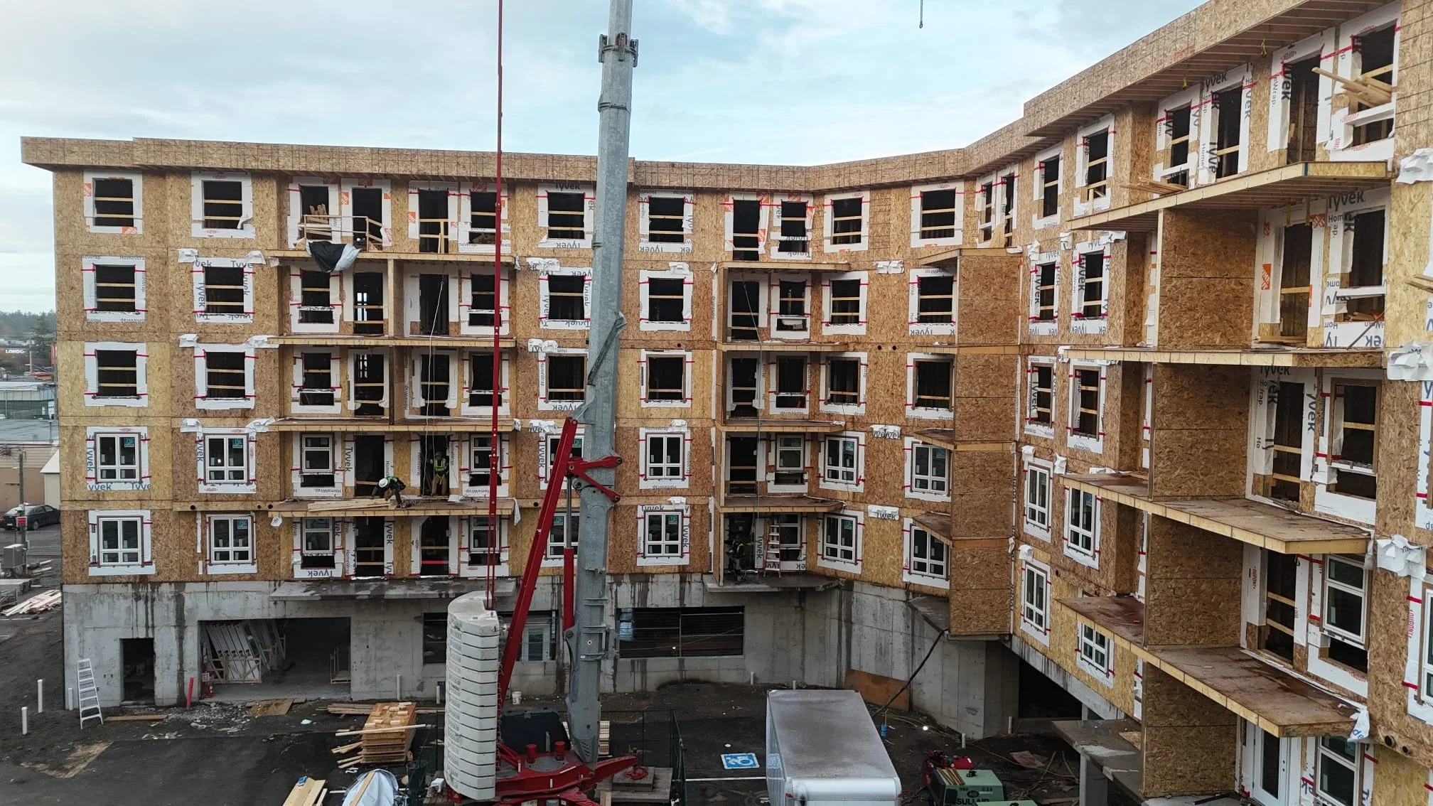 A multi-story building under construction with workers on the balconies and a construction crane in the foreground.