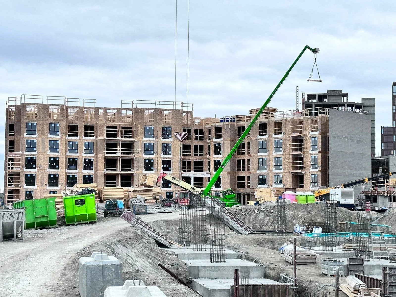 Construction site with a partially built multi-story building, green cranes, construction materials, and equipment.