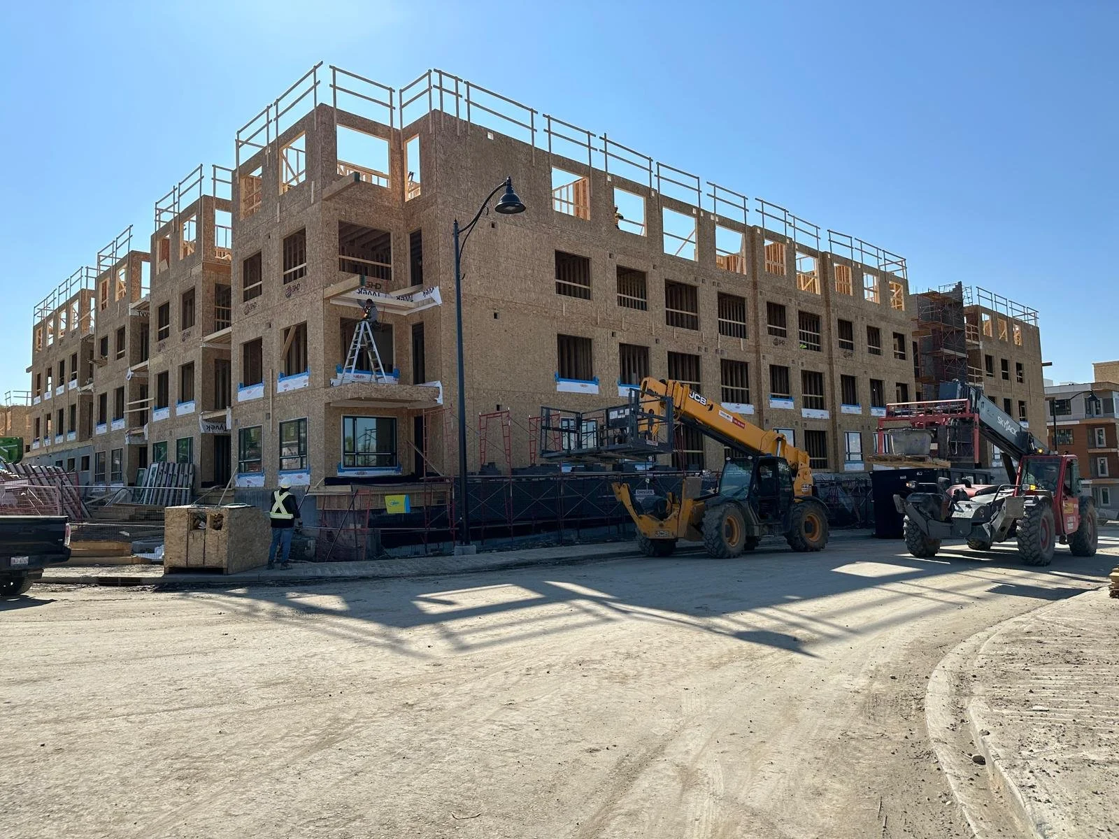 Construction site of a multi-story building with scaffolding, construction workers, and machinery on a sunny day.