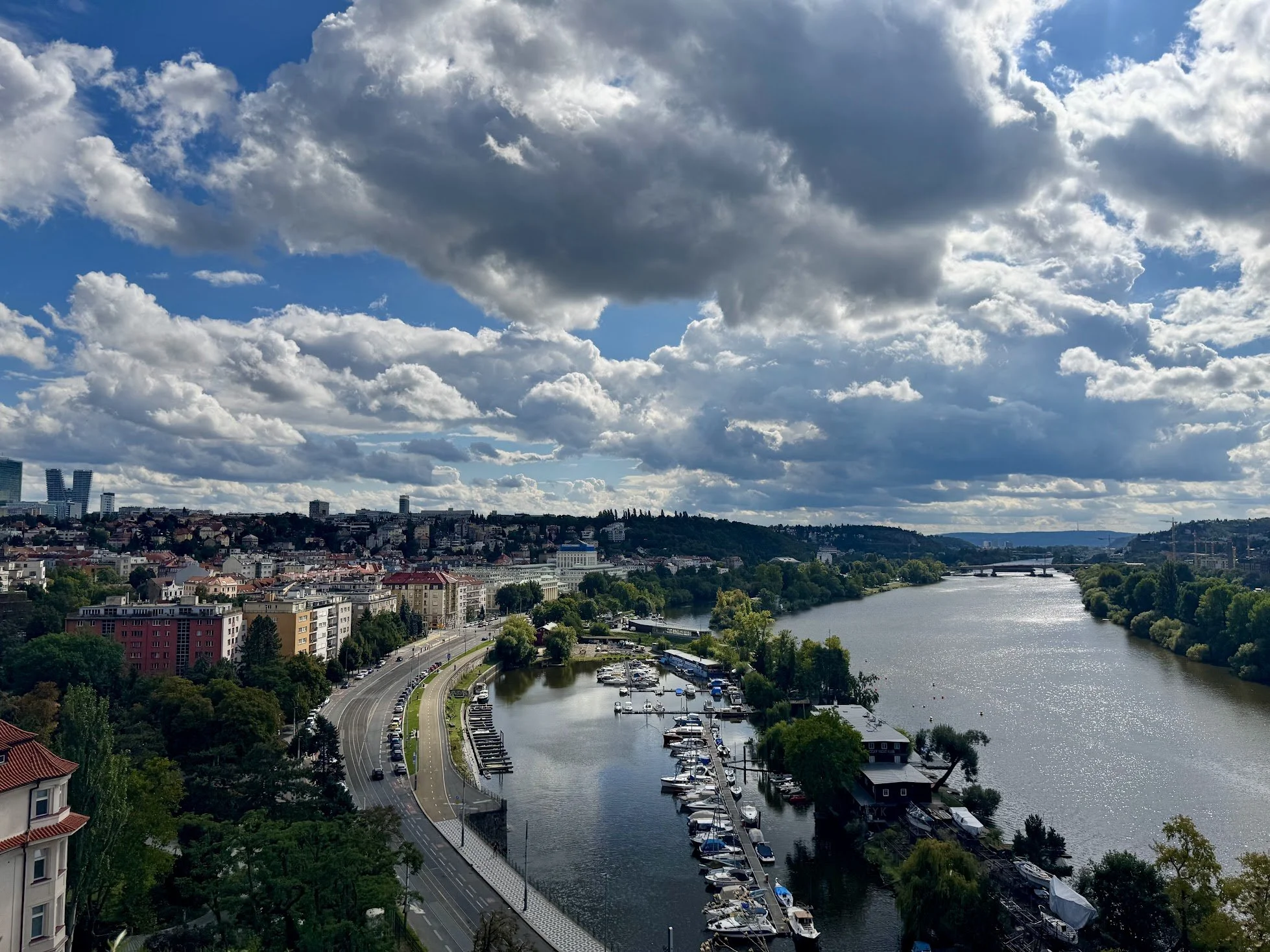 Cityscape with a river, boats, buildings, and a partly cloudy sky.