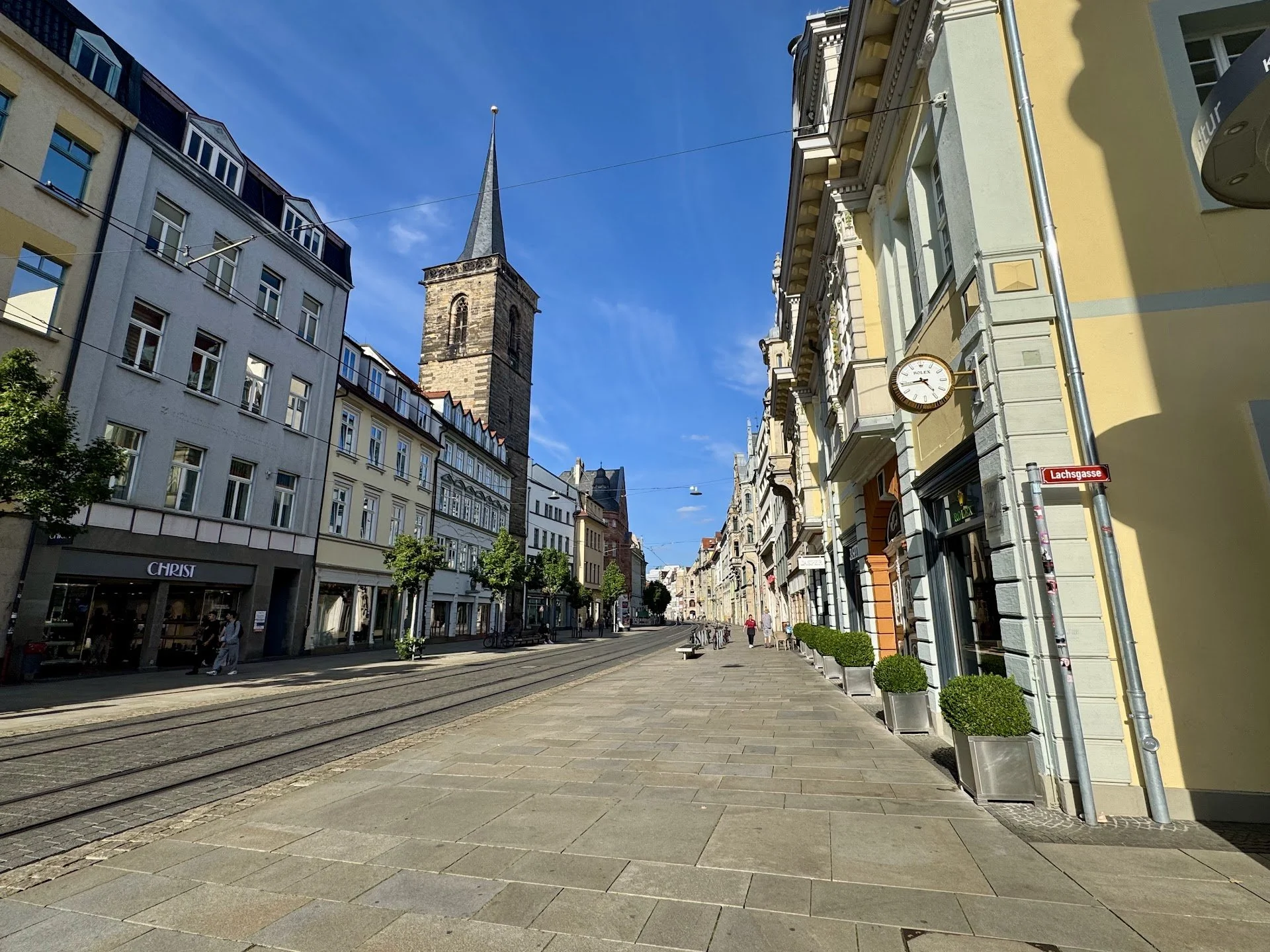 European city street with historic buildings, a church tower, tram tracks, and a clock on a yellow building.