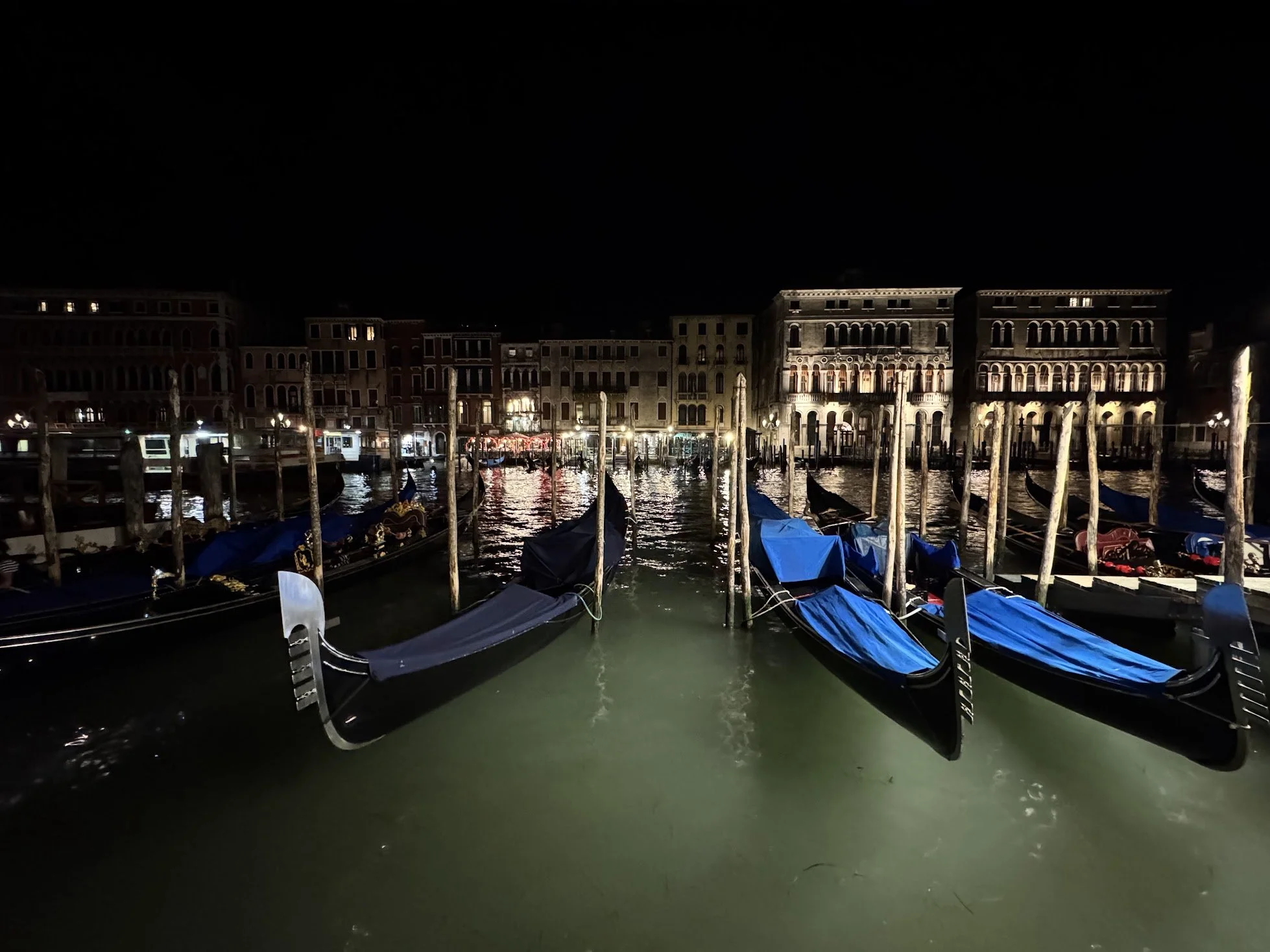 Nighttime view of Venice, Italy with gondolas docked on the water, old buildings along the canal, and illuminated street lights.