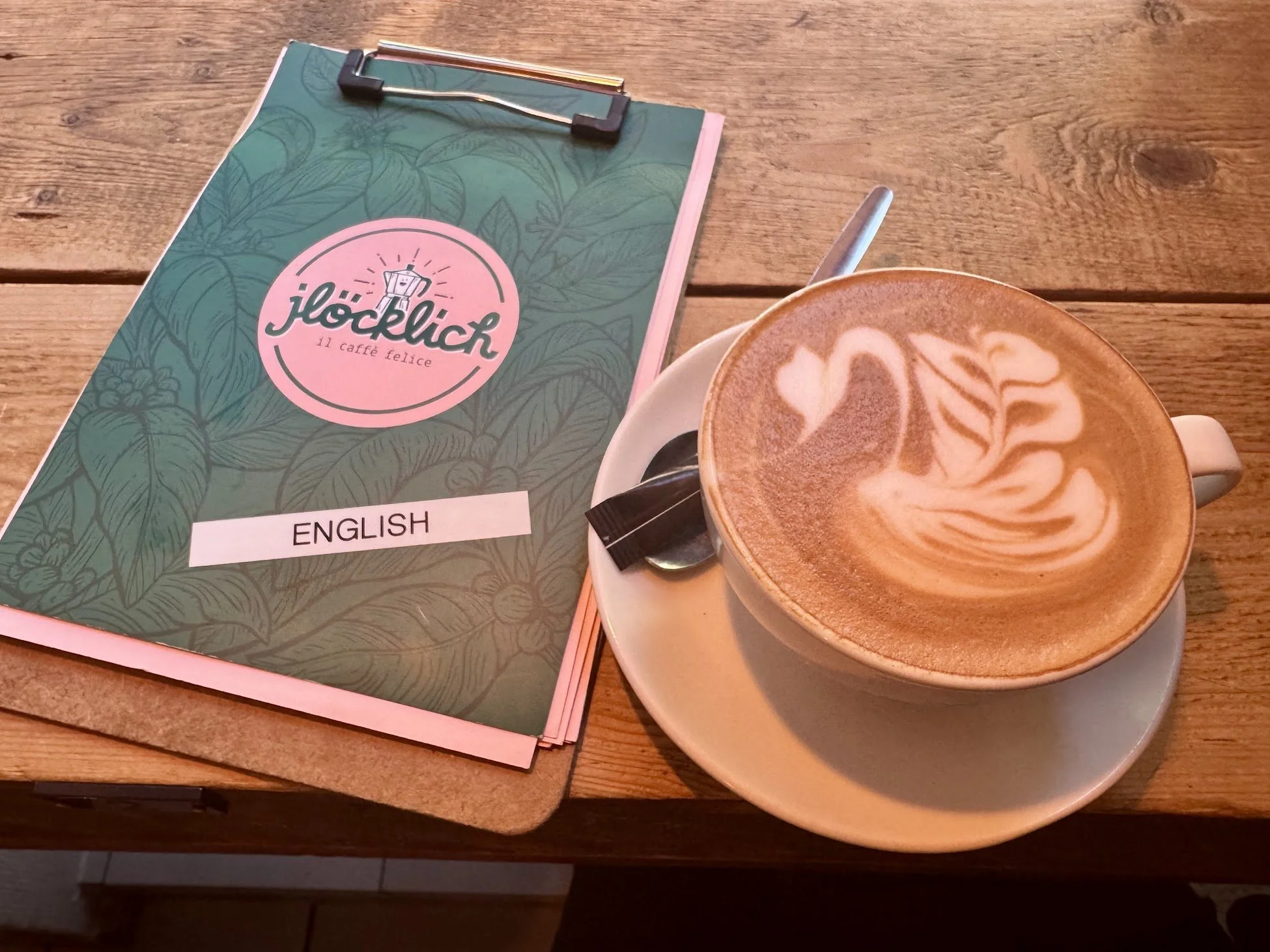 A wooden table with a menu and a cup of latte art coffee.