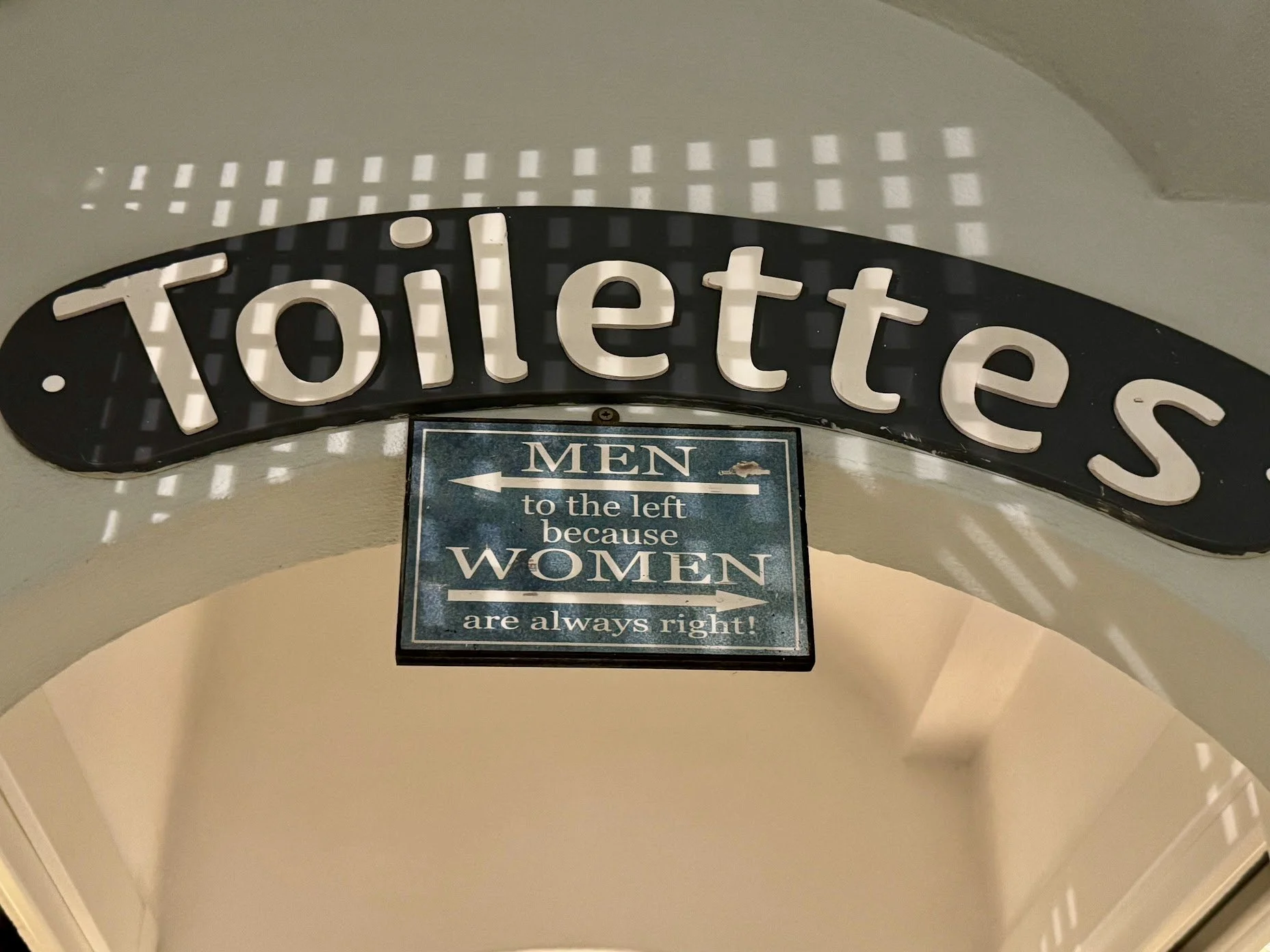 Sign reading 'Toilets' with an additional sign below indicating directions for men's and women's restrooms.