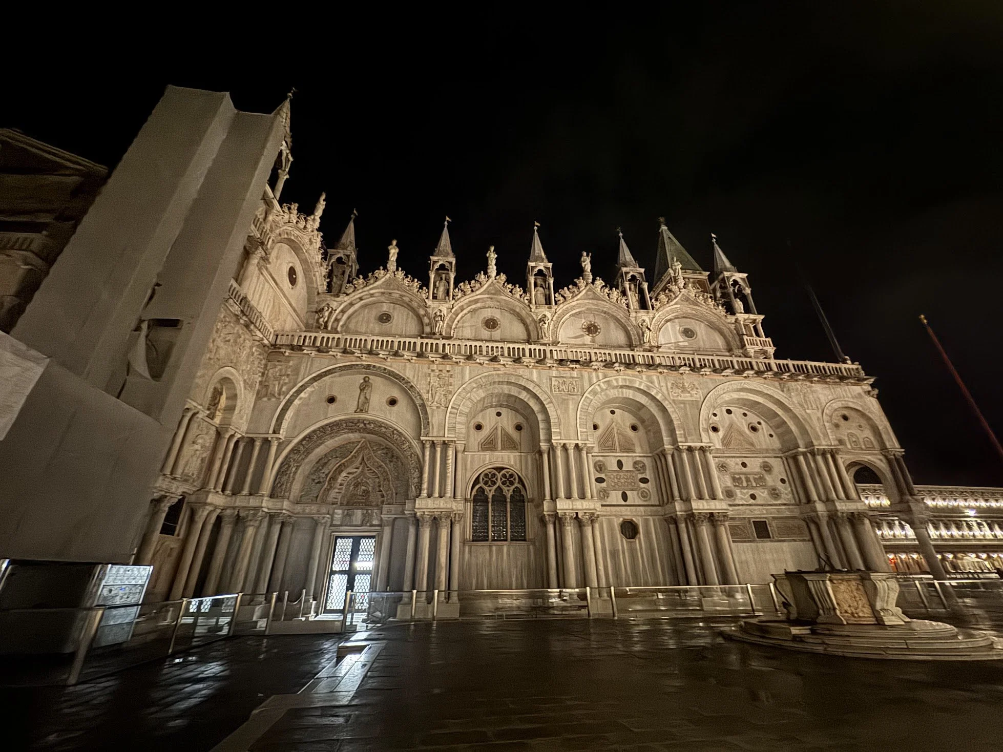 Photo of the front of a Gothic cathedral at night, illuminated and featuring ornate architectural details, including pointed arches and statues.
