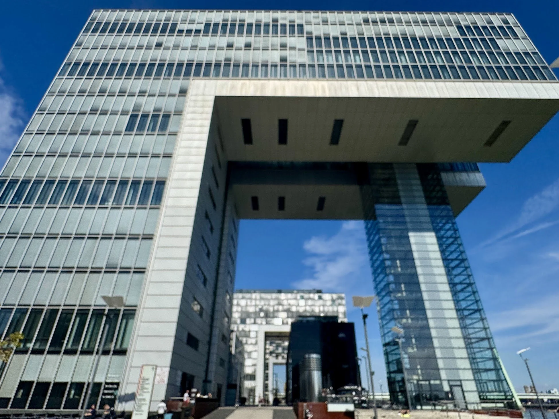 Modern multi-story office building with glass facade and distinctive cantilevered section, under a clear blue sky.