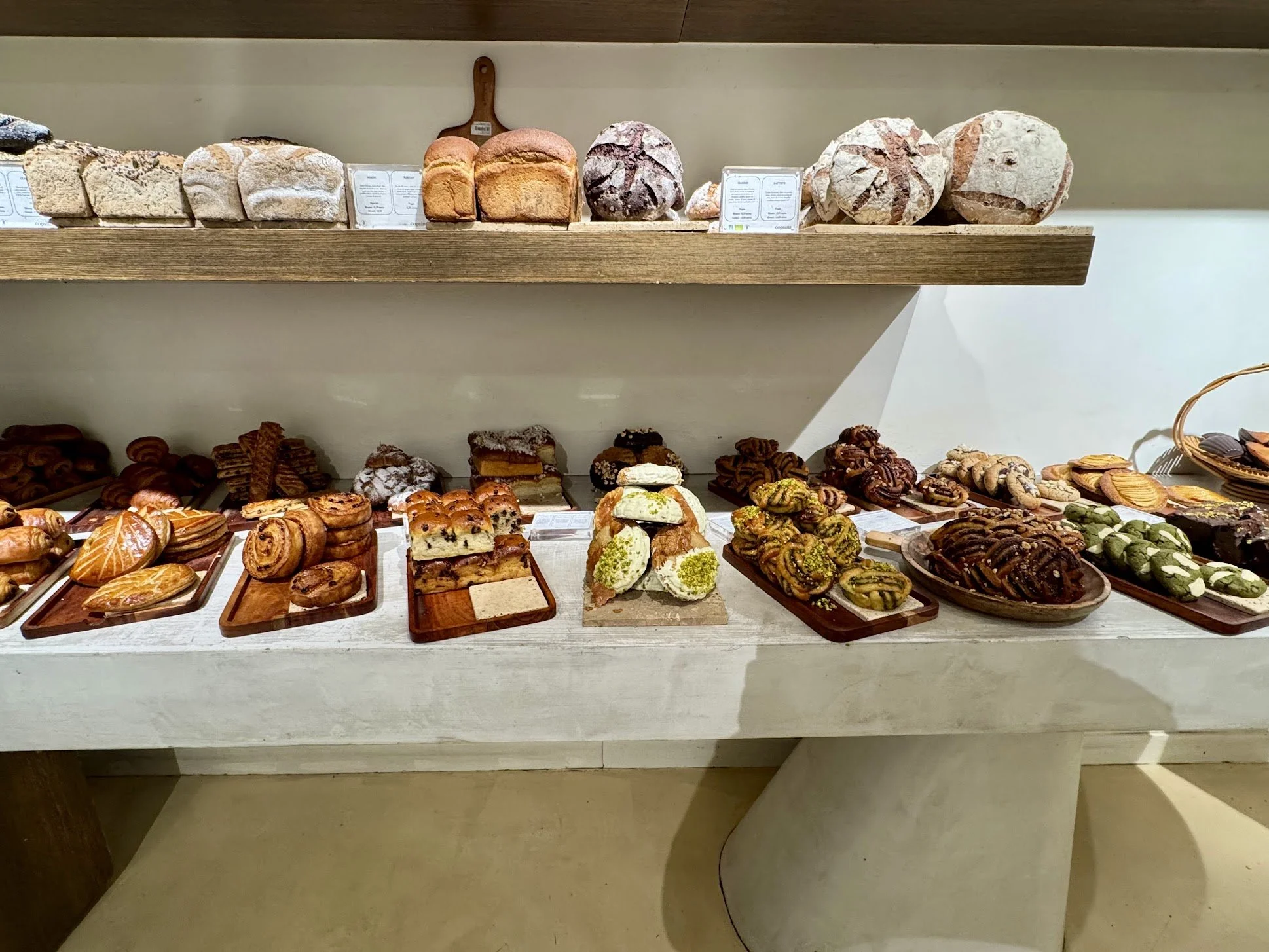 Assorted baked goods, including bread, cookies, and pastries, arranged on a display shelf in a bakery.