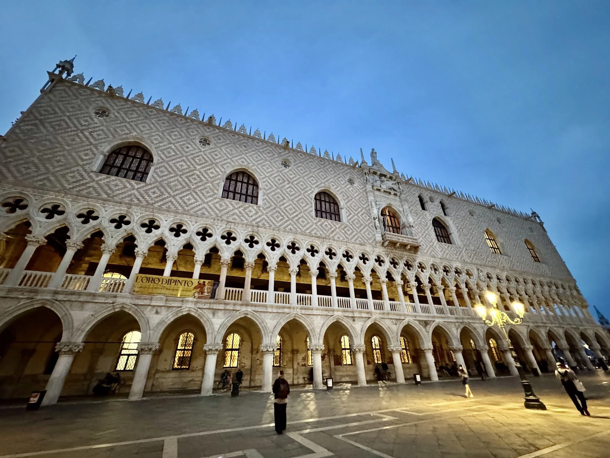 Night view of a historic European building with ornate architectural details, arched windows, columns, and small statues on top, under a clear blue sky.