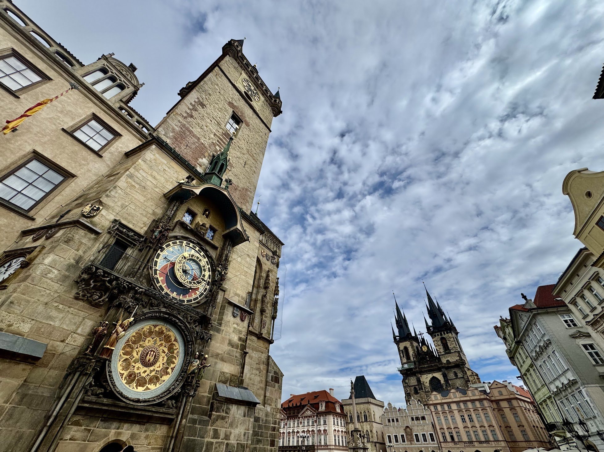 Historic clock tower and cathedral in a European city, cloudy sky, old buildings, and gothic architecture.