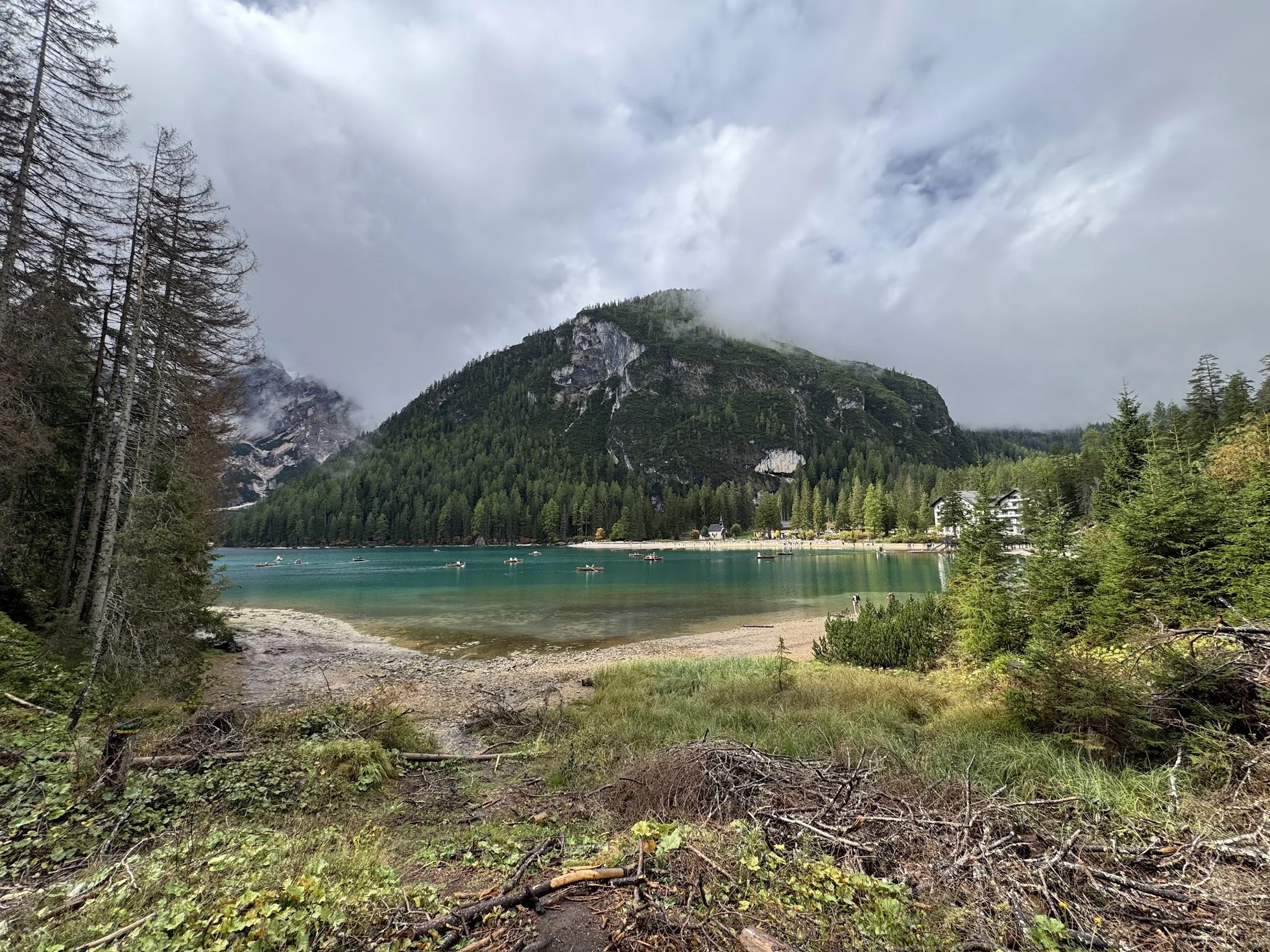 A scenic mountain landscape with a lake, trees on the shoreline, and clouds covering the mountain top.