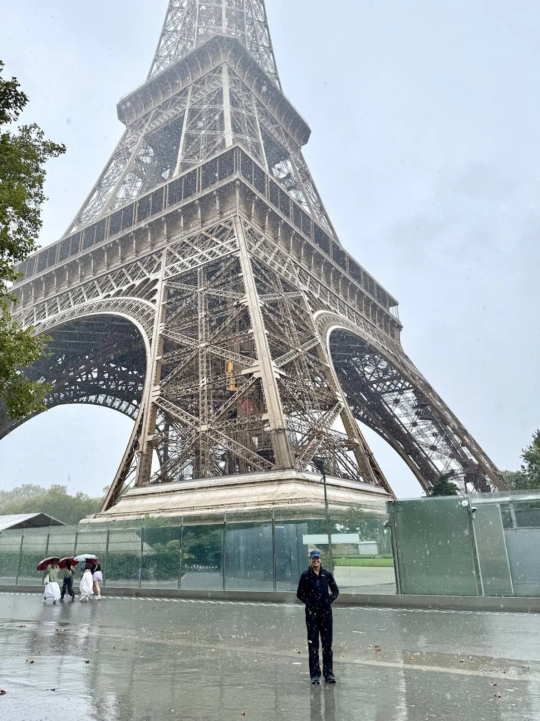 People walking with umbrellas near the base of the Eiffel Tower in rain.