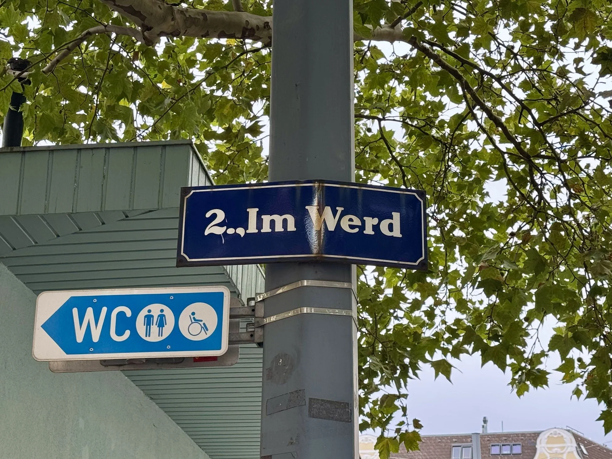 Street sign reading '2.Im Werd' against a background of green trees and a building with a sloped roof.