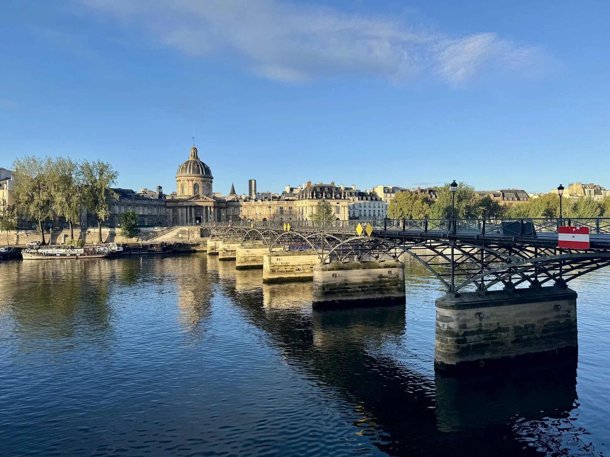 A scenic view of the city skyline along the River Seine in Paris, featuring historic buildings, a dome, and a bridge crossing the river.