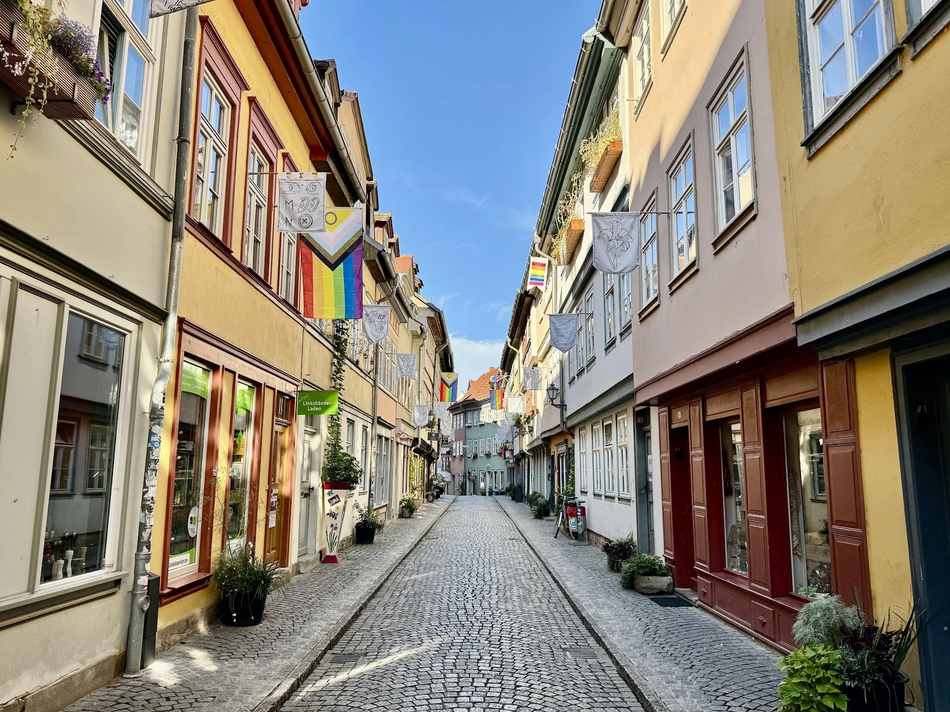 A narrow European street with colorful buildings, flower boxes, and hanging flags.