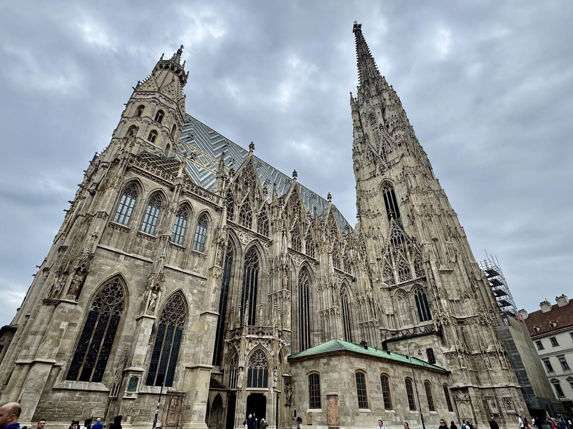 Front view of a historic Gothic cathedral with detailed stone carvings and large stained glass windows, featuring soaring spires and a cloudy sky in the background.