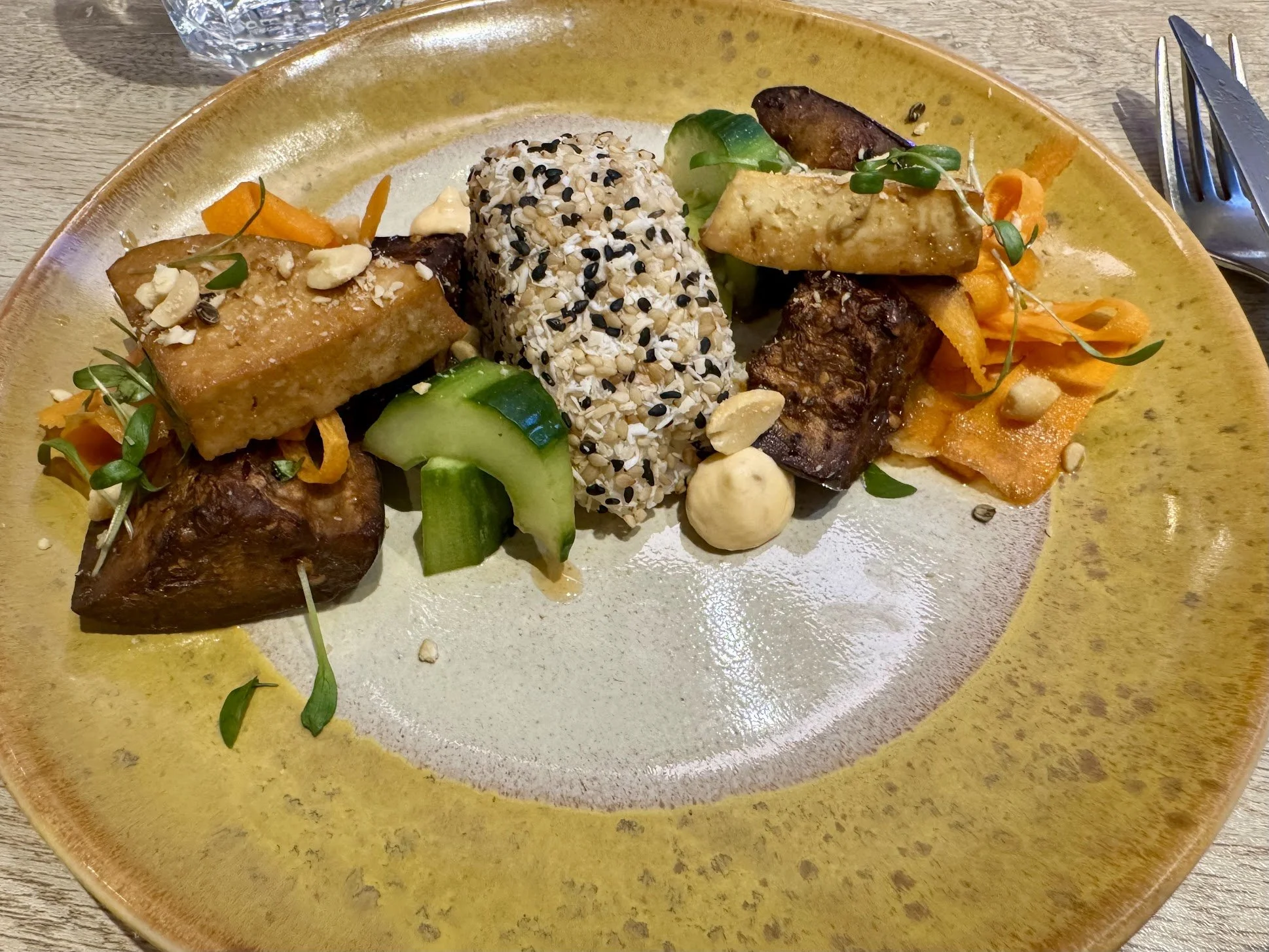 A plate of assorted vegan dishes including tofu, vegetables, and grains, garnished with sprouts and nuts.
