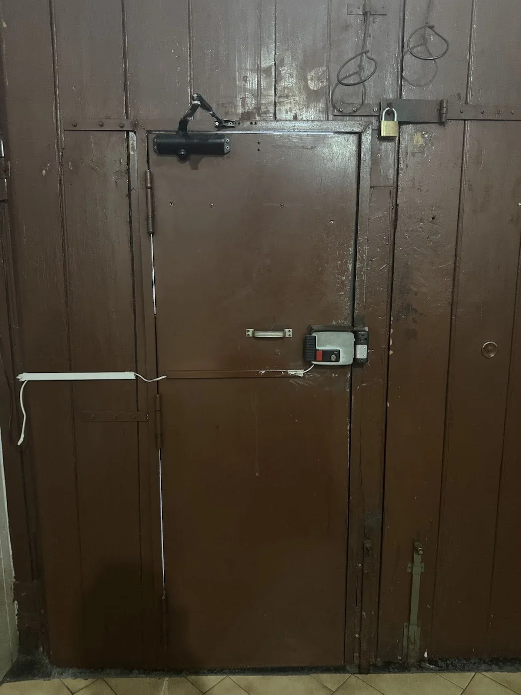Brown wooden door with a small lockbox, door handle, padlock, black latch, and electrical wiring.