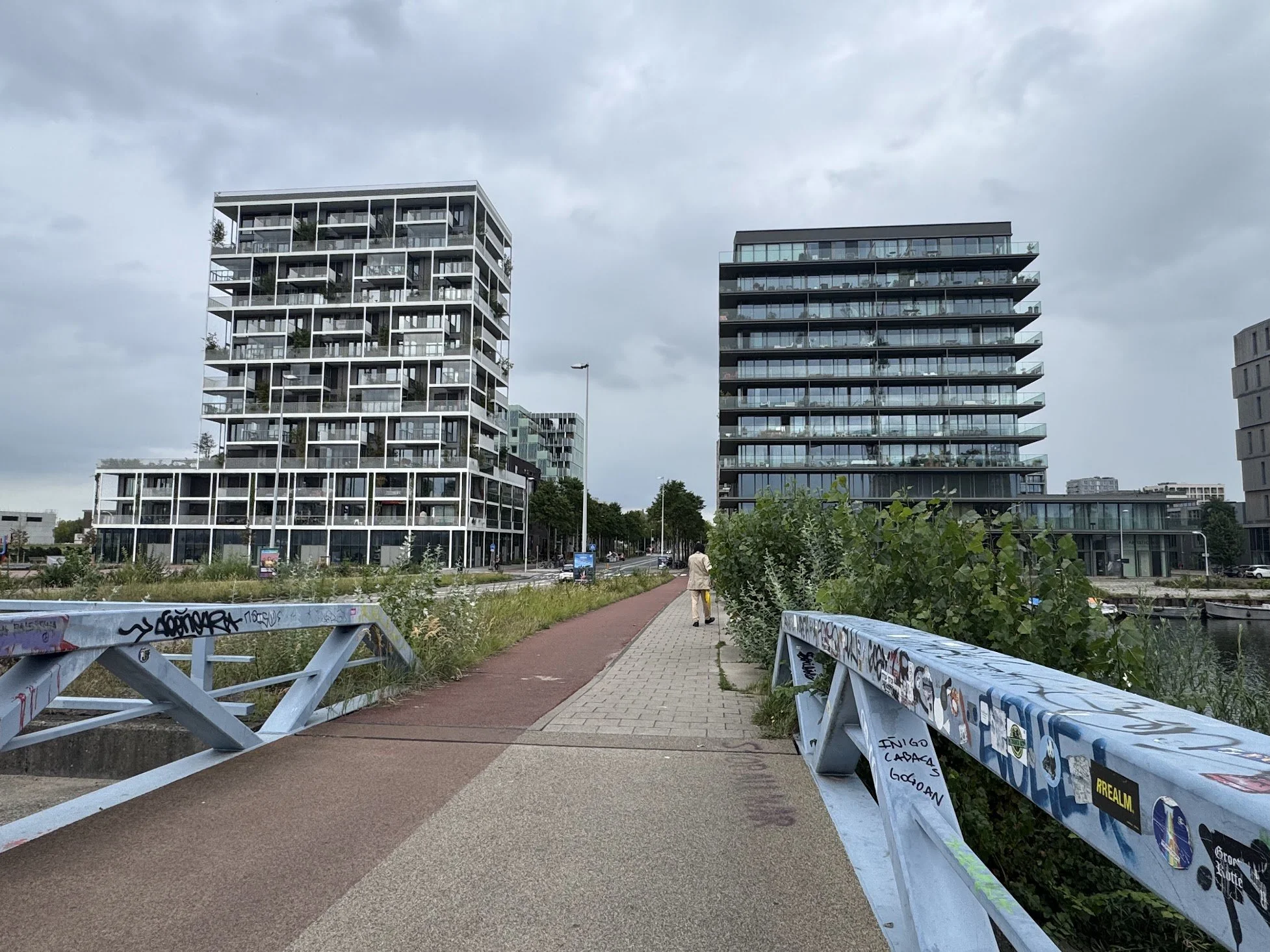 Urban scene with modern apartment buildings, a sidewalk, and graffiti-covered benches, under a cloudy sky.