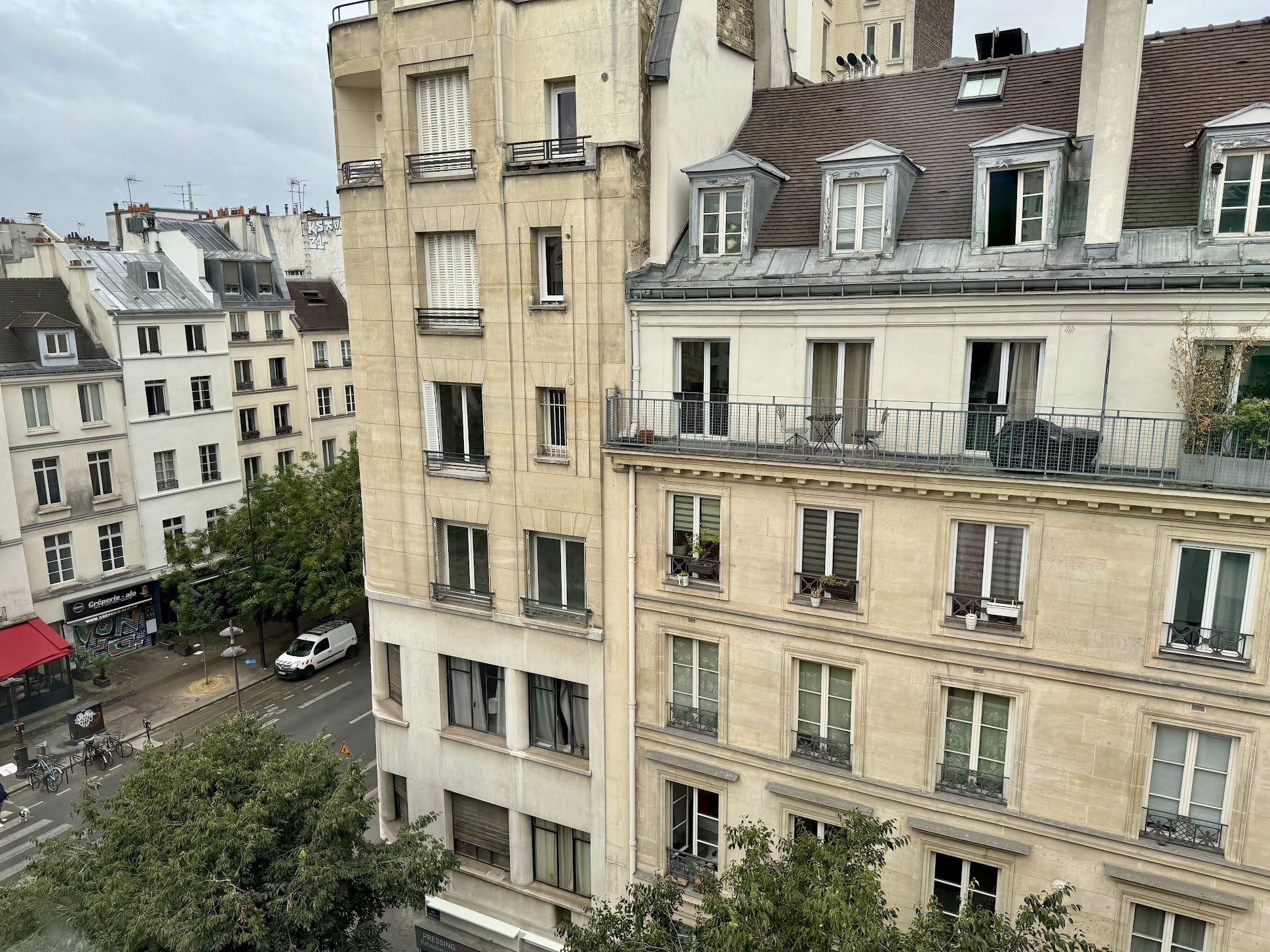 Photo of Parisian apartment buildings with classic architecture, including dormer windows and balconies, under a cloudy sky.