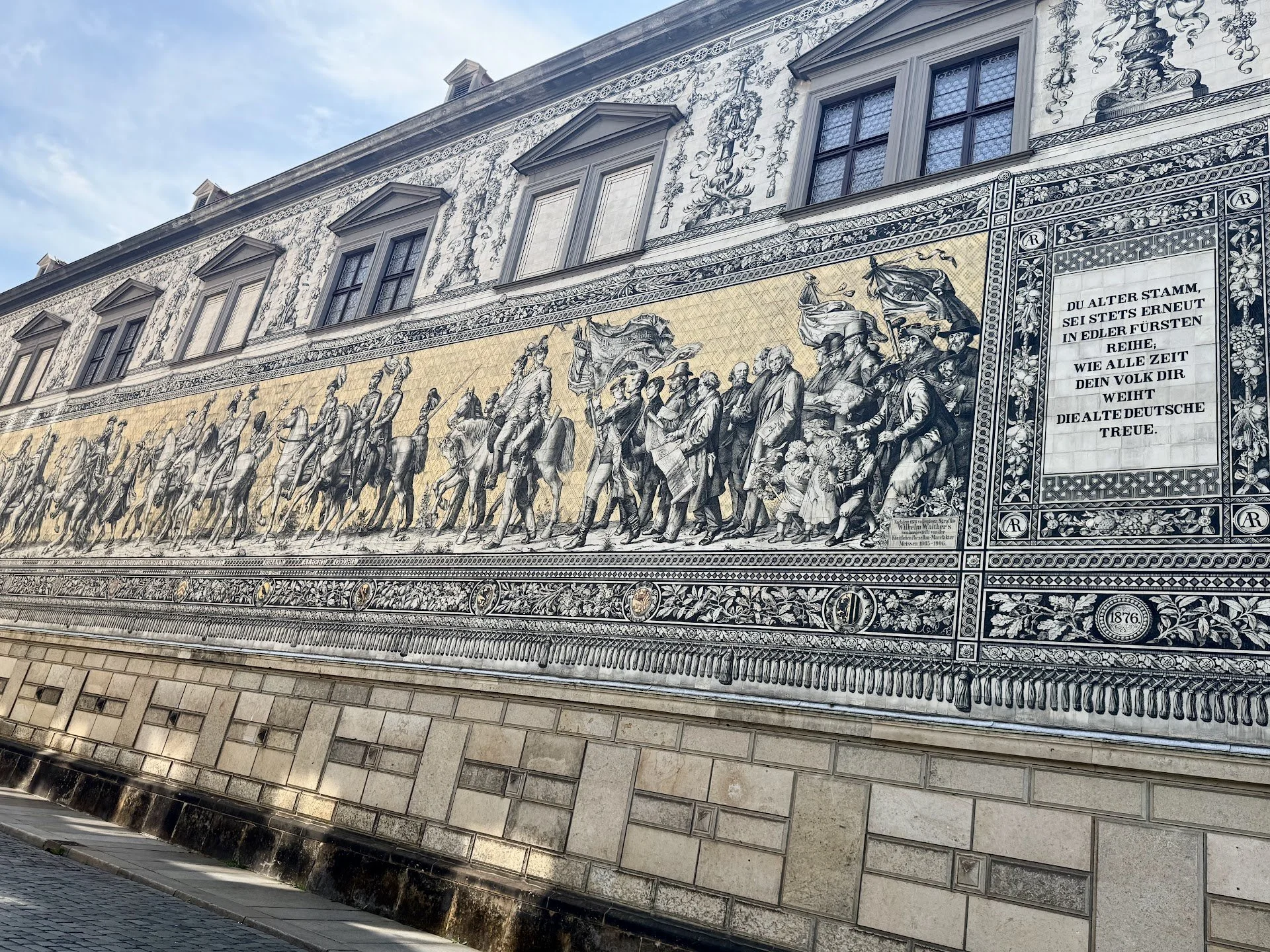 A large decorative mural and historic building exterior with detailed artwork, including a row of marching soldiers and a block of German text, located in Germany.