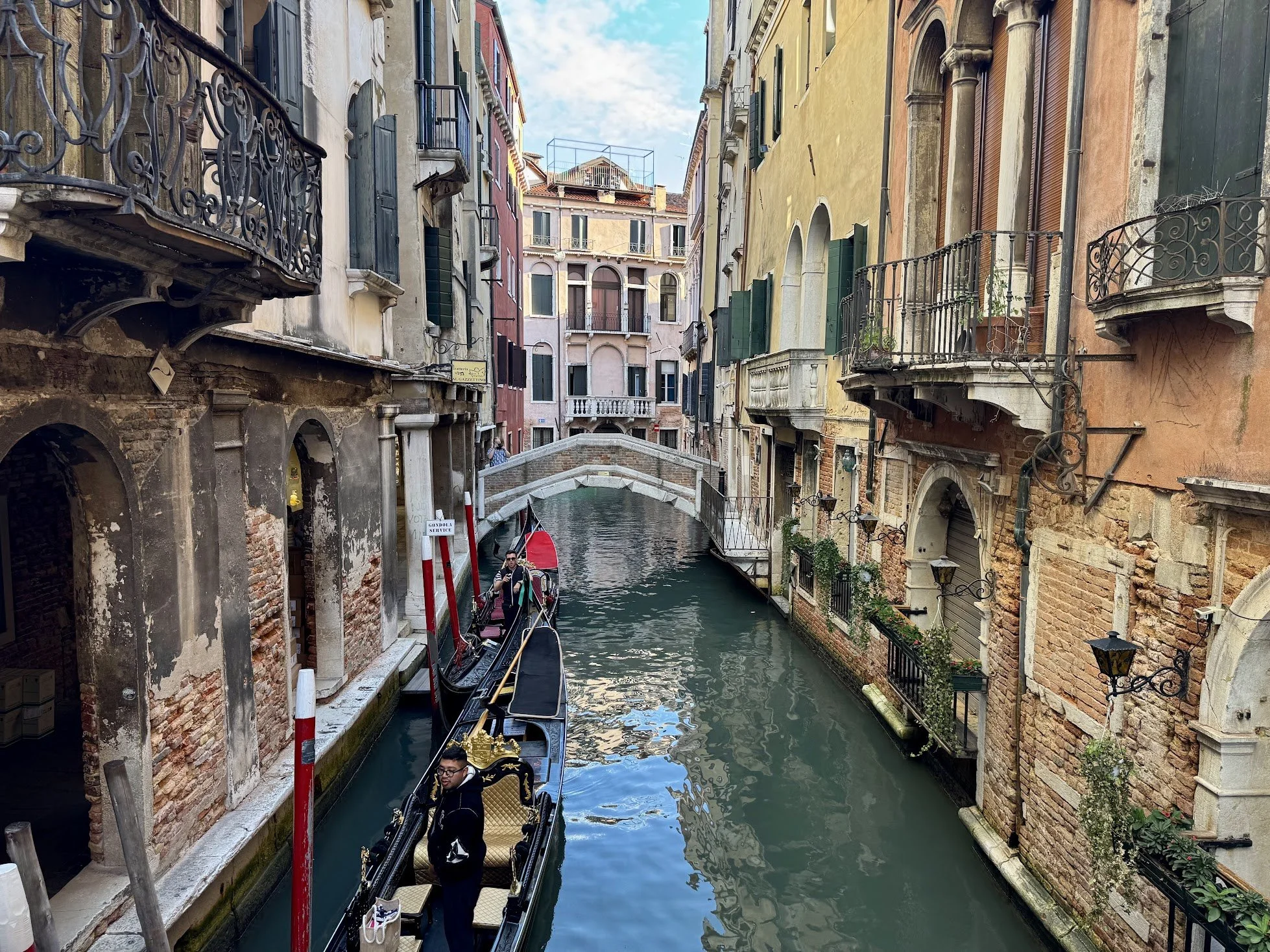 Gondola boat floating in a narrow canal with colorful old buildings lining both sides, balconies, and windows, in Venice, Italy.