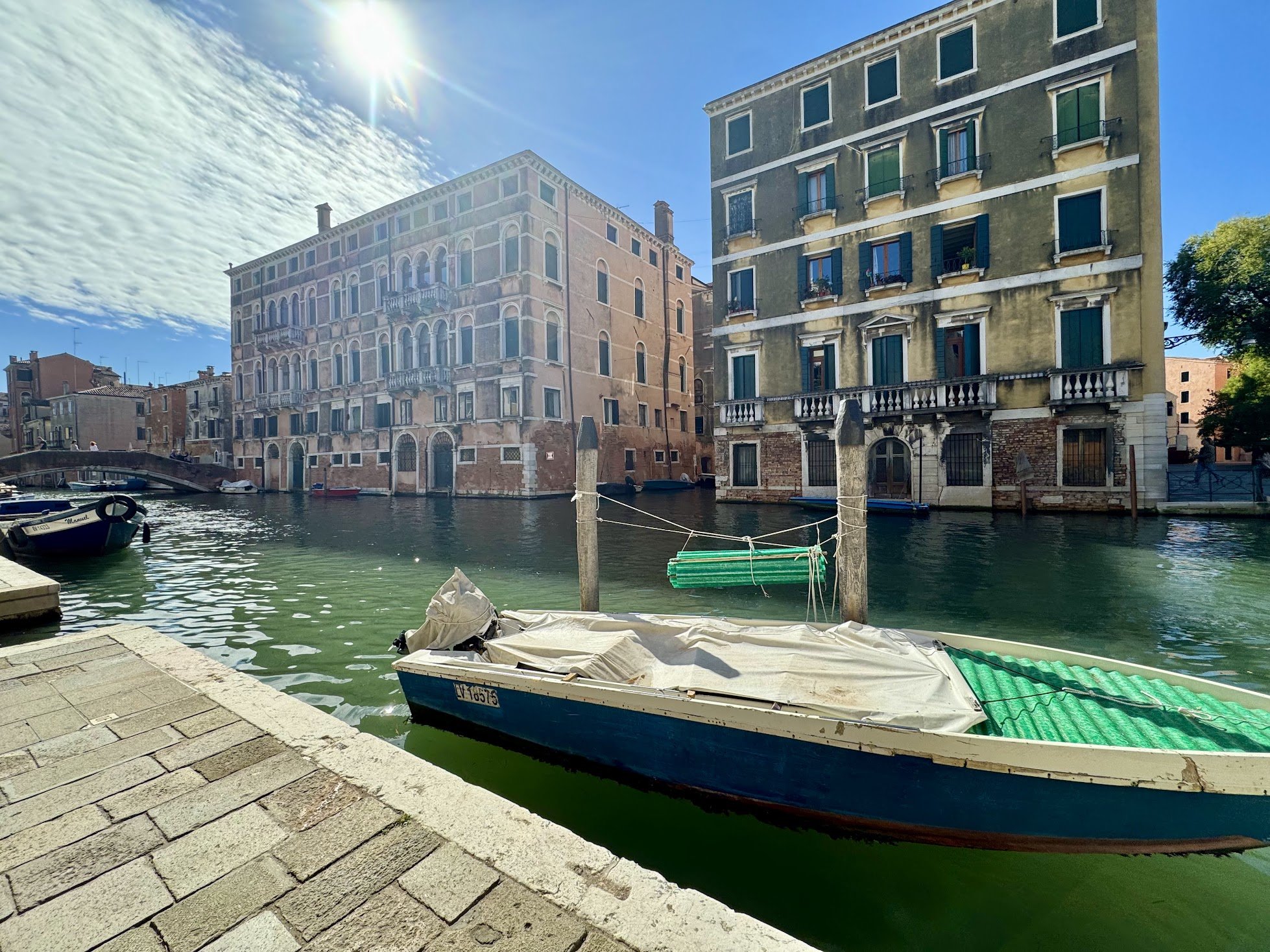 View of historic buildings alongside a canal with boats in Venice, Italy on a sunny day.