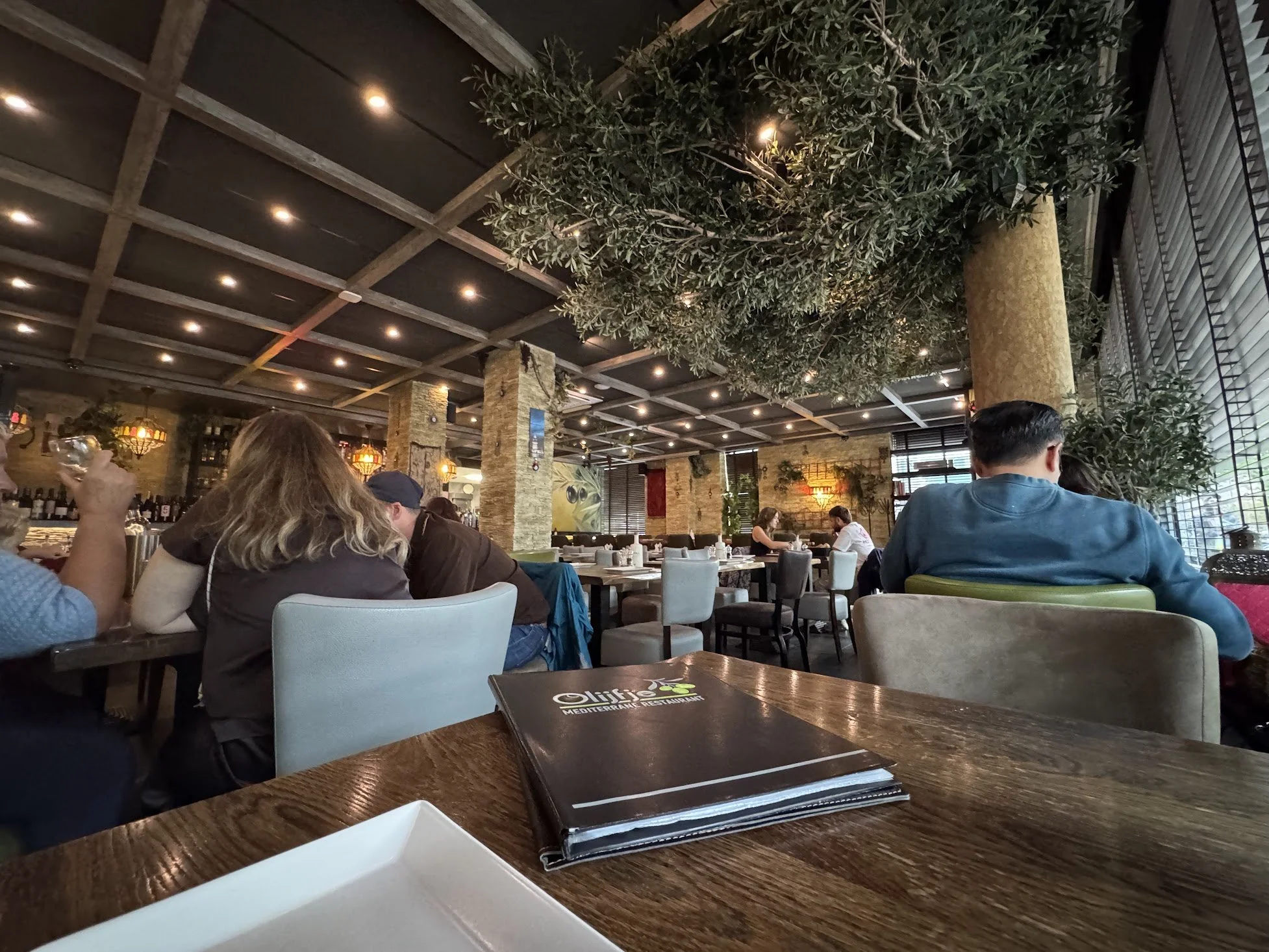 Interior of a restaurant with people sitting at tables, a large tree in the center, and decorative ambient lighting.