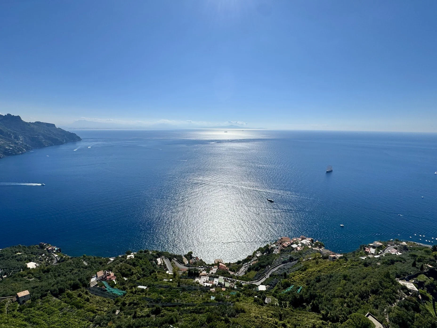 A picturesque view of a coastal landscape with blue ocean water, multiple boats, green hills, and residential houses.