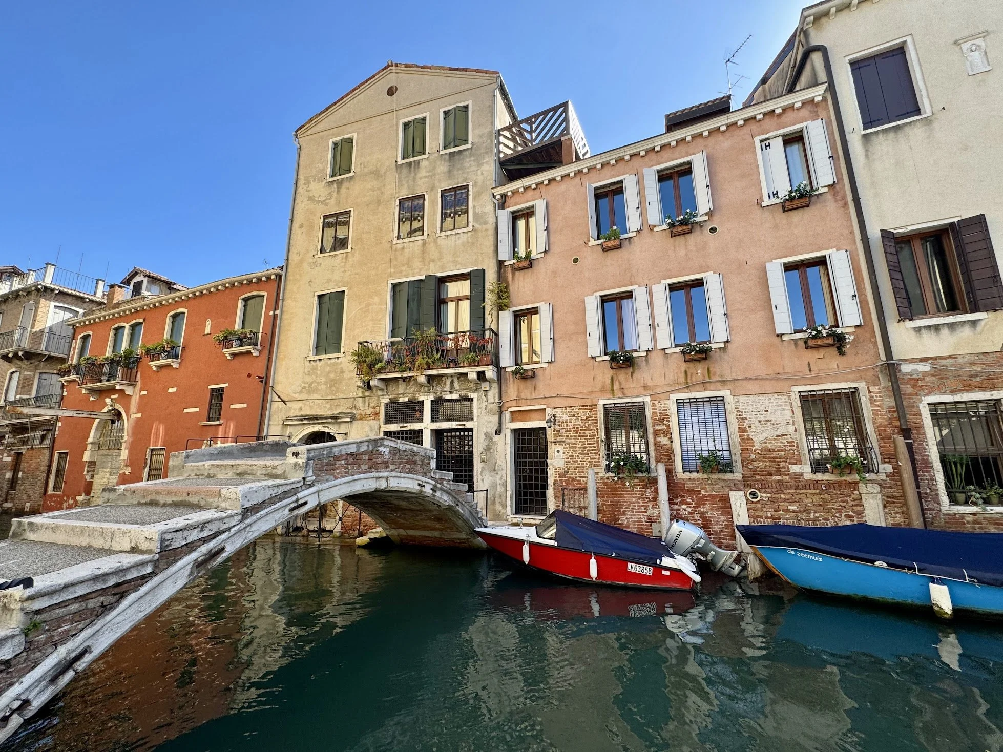 Colorful buildings along a canal in Venice, Italy, with a small stone bridge and boats in the water.