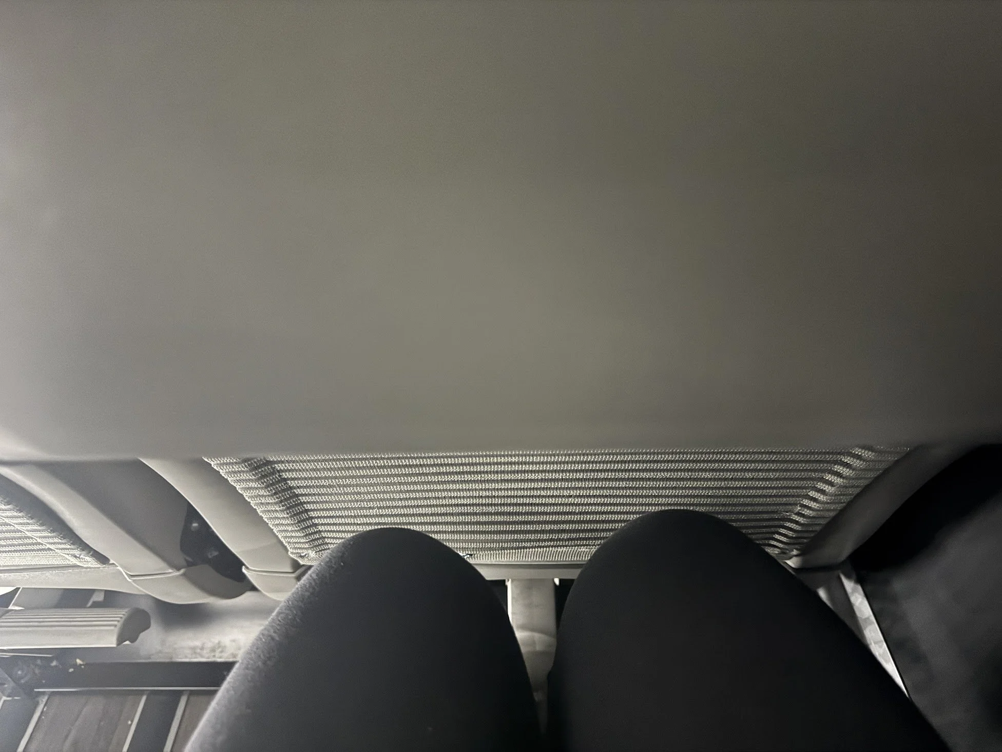 View of an airplane seat from the passenger's perspective, showing two black seats and a gray overhead compartment.