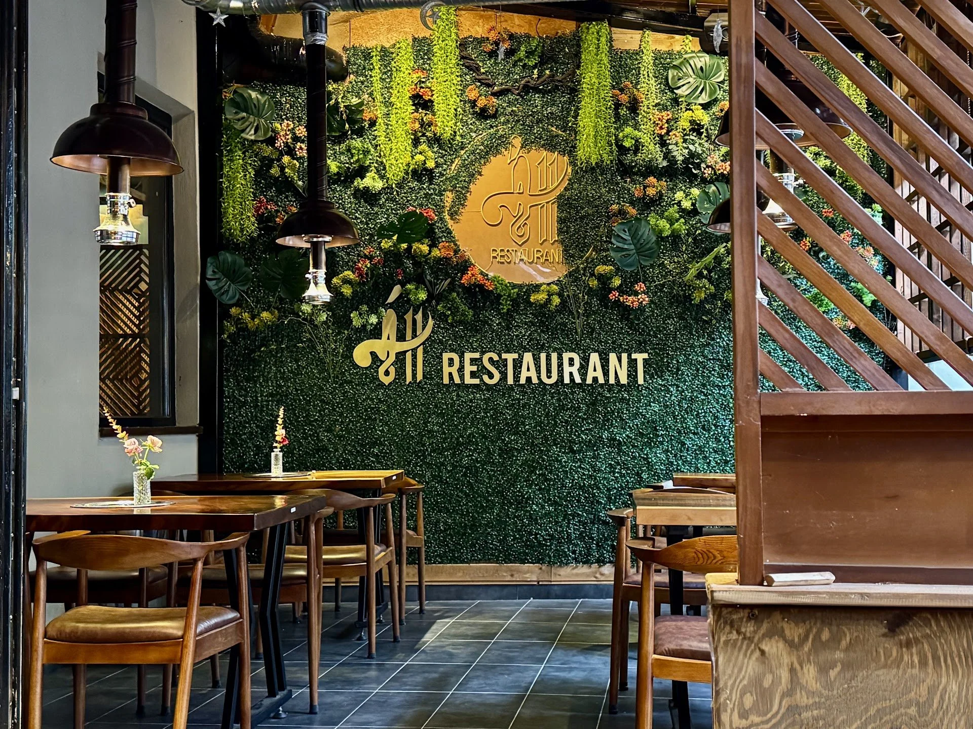 Interior of a restaurant with wooden furniture, a green wall with plants and a yellow sign that reads "Restaurant".