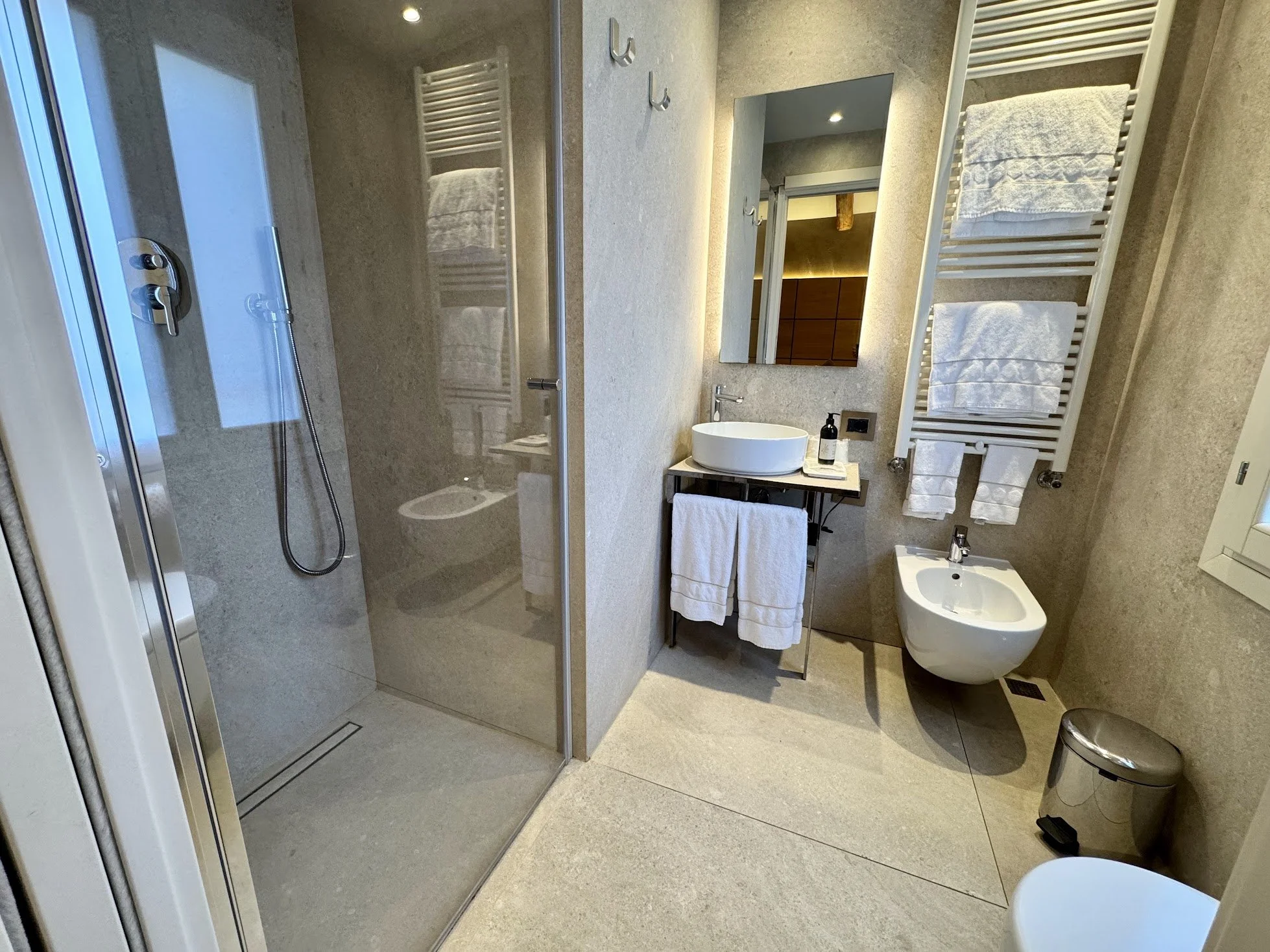 Modern bathroom with a walk-in shower, a sink with a mirror, and towel racks with towels.