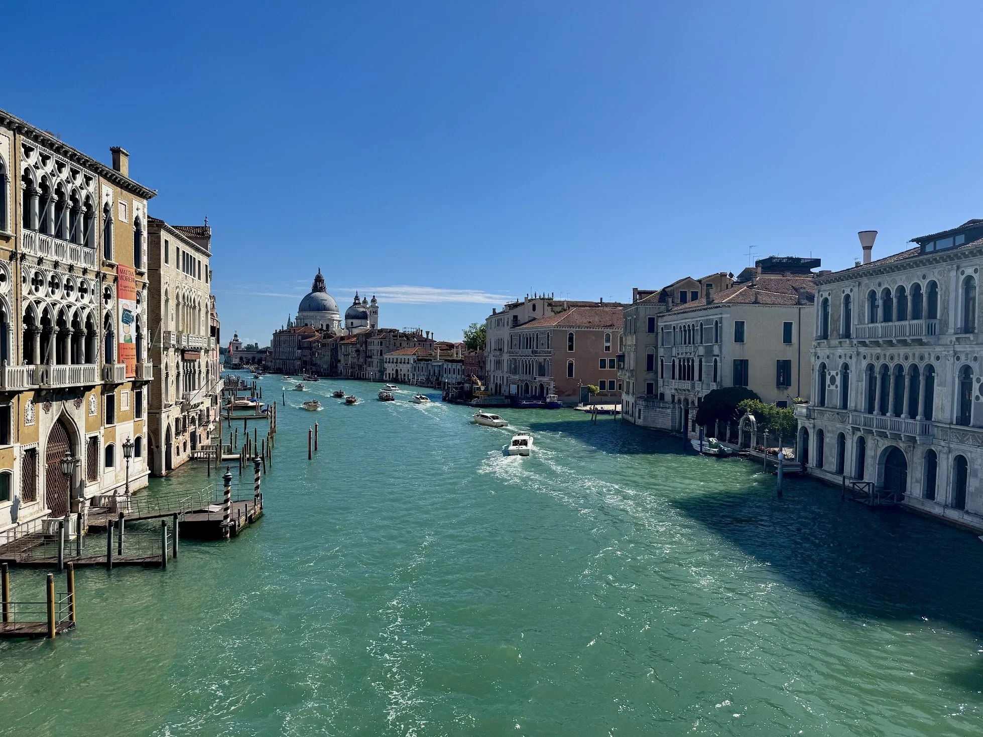 Venetian canal with boats and historic buildings under a clear blue sky.